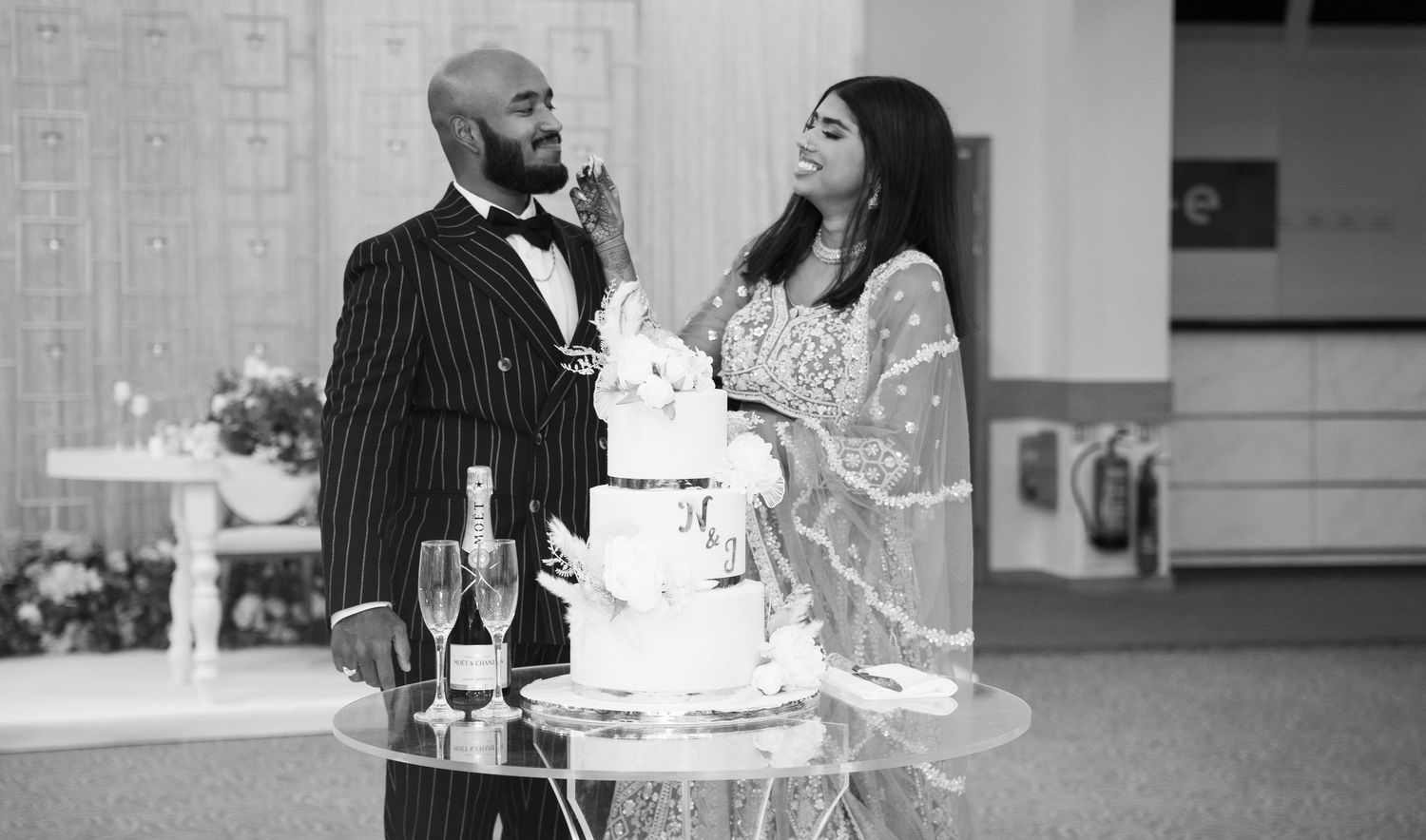 Black and white photo of couple sharing cake feeding moment at wedding reception.