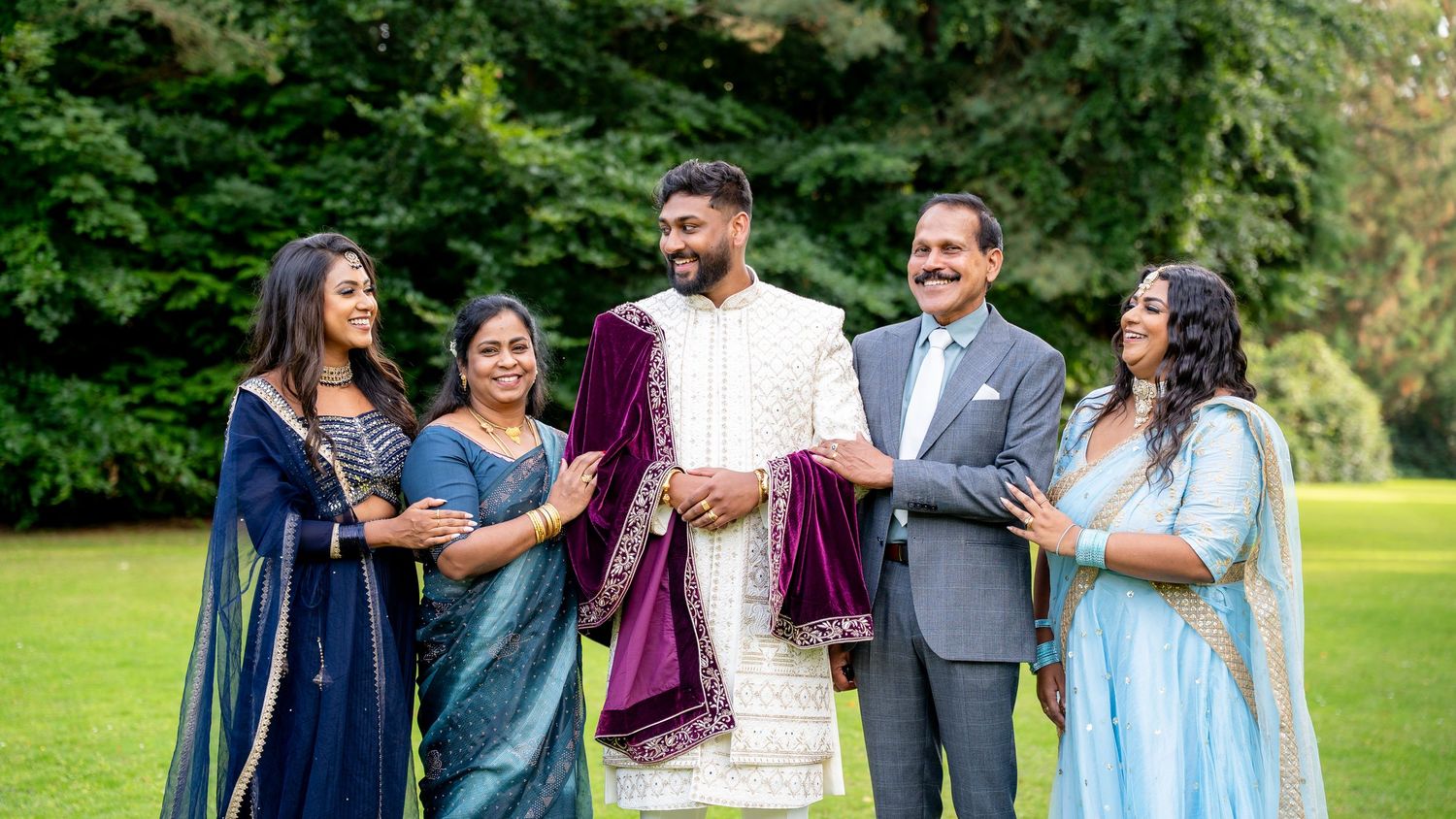 Indian family in traditional attire celebrating a wedding outdoors on lush green grounds.