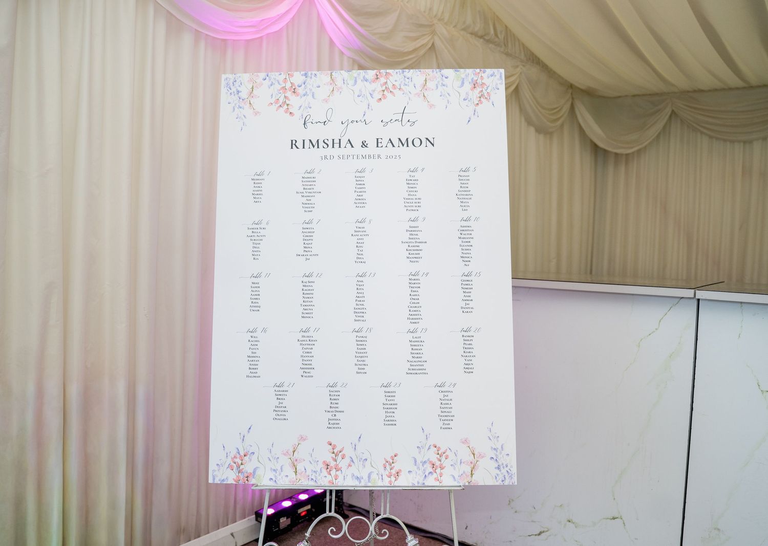 Elegant wedding seating chart on easel with floral border displaying guest table assignments for Rimsha and Eamon.