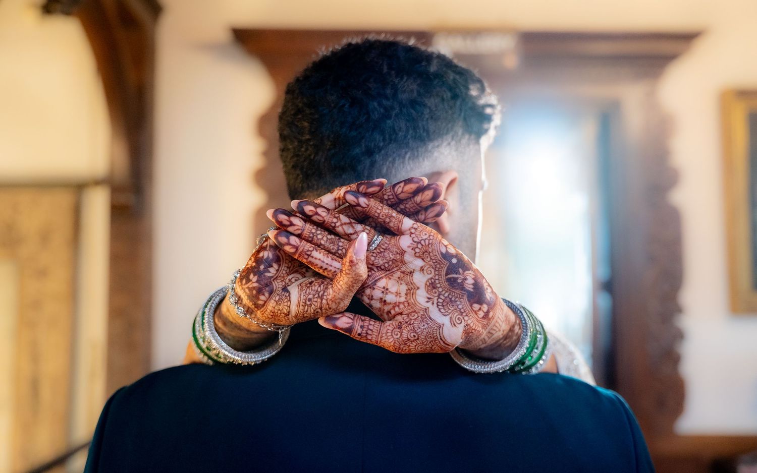Close-up of bride's henna-decorated hands clasped around groom's neck at South Asian wedding ceremony.
