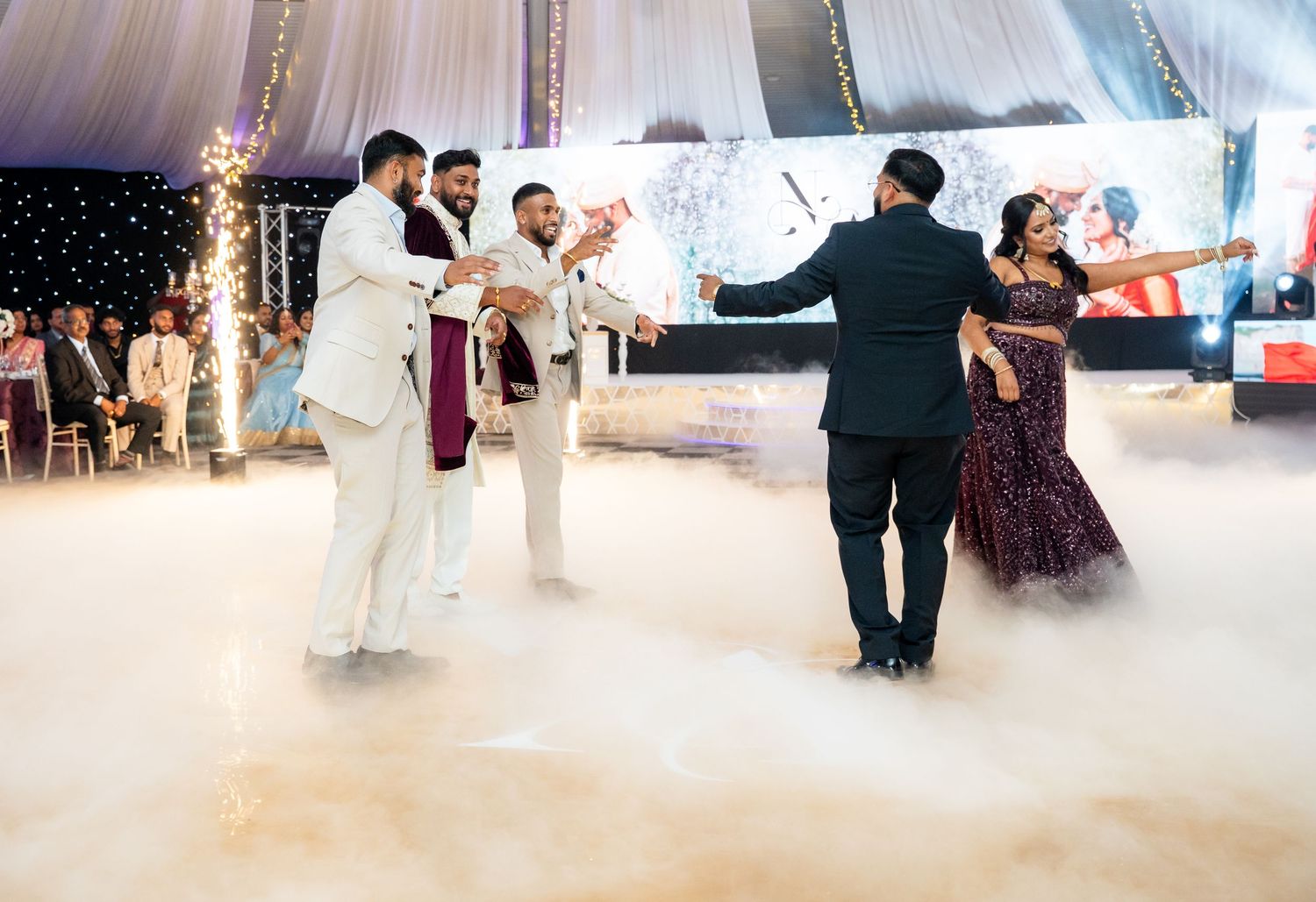 Couples dancing on a foggy dance floor at an elegant Indian wedding reception with sparkling lights.