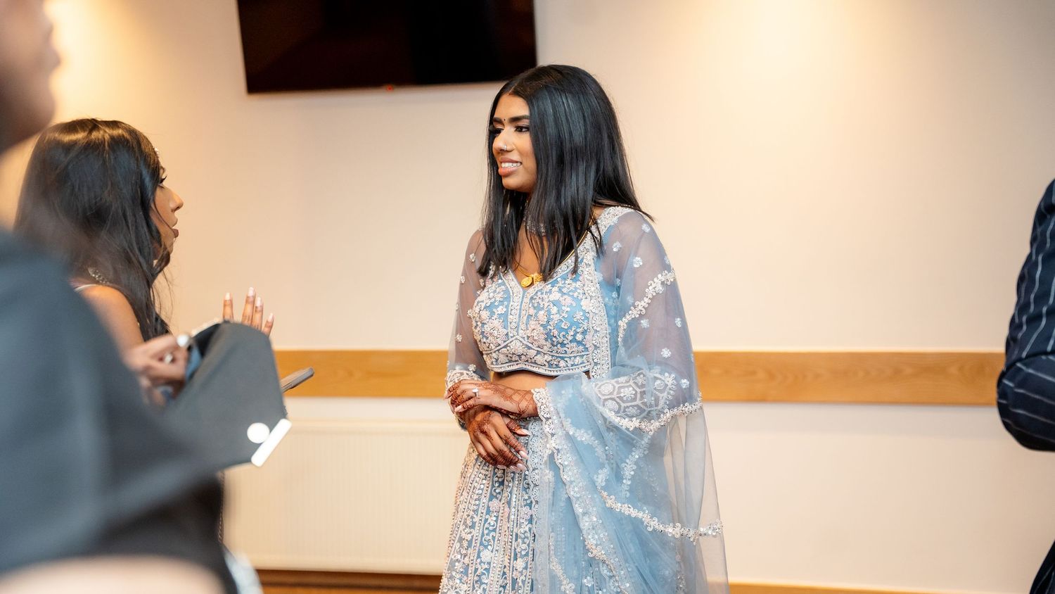 Woman in light blue Indian lehenga smiles warmly while socializing at a formal event.