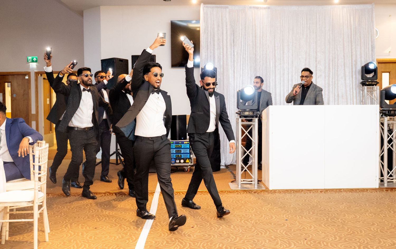 Groomsmen in black suits performing a choreographed dance routine at an elegant wedding reception.