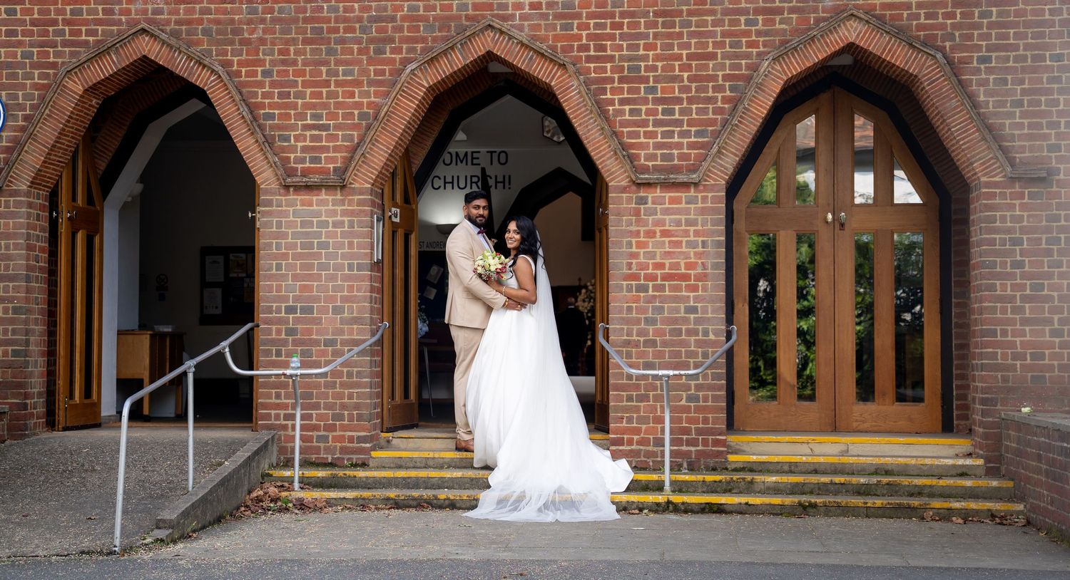 Bride and groom posing at church entrance with brick arches on their wedding day.