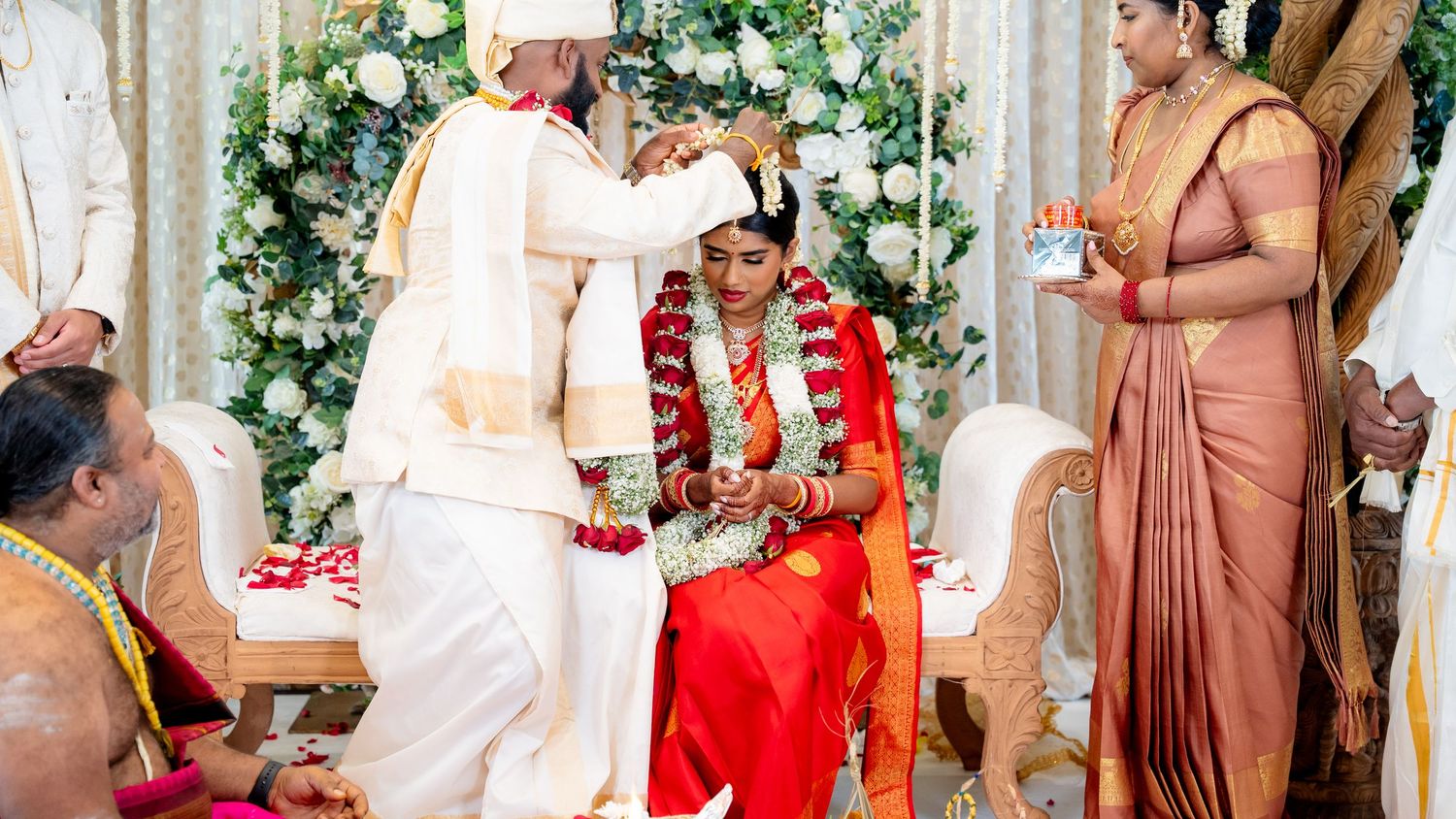 Groom applies vermillion to bride during traditional South Indian Hindu wedding ceremony on stage.