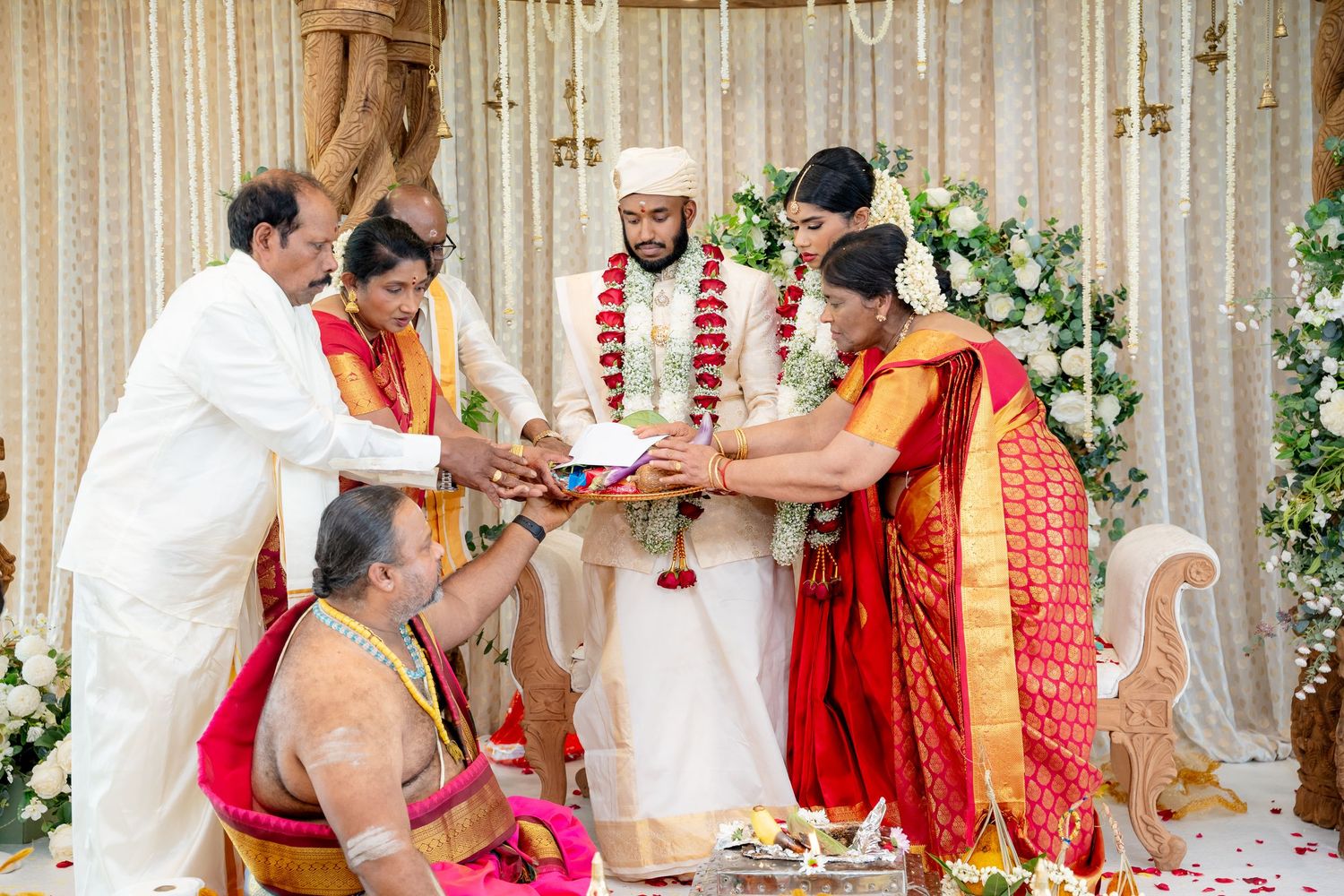 Family members and priest gather hands together in sacred South Indian Hindu wedding ritual at decorated mandap.