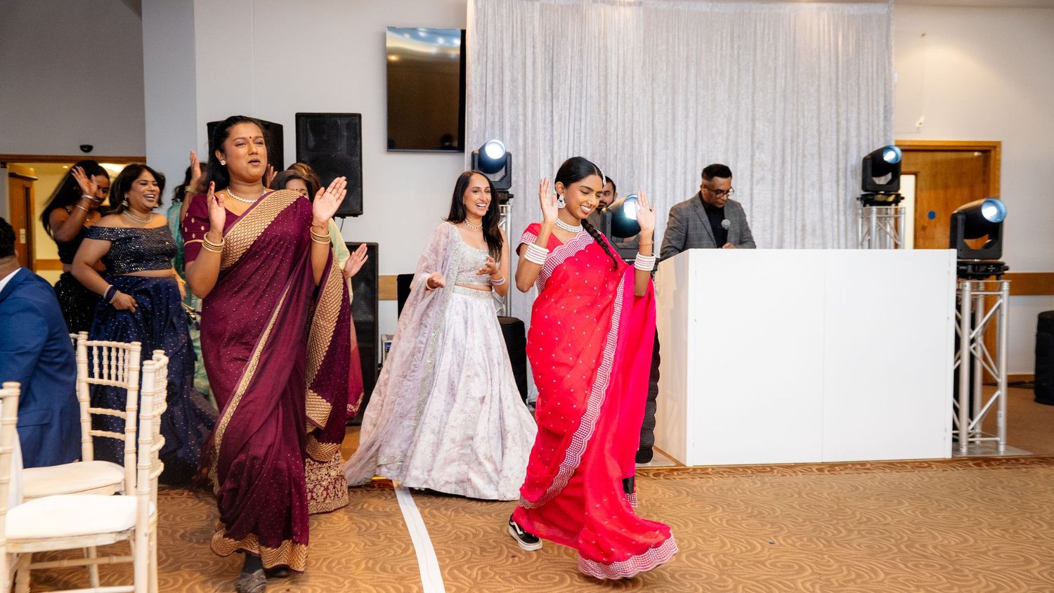 Three women in traditional sarees performing a dance near the DJ booth at a wedding.