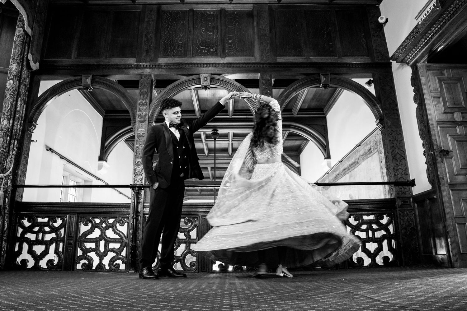 Black and white photo of bride and groom dancing at a grand historic wedding venue.