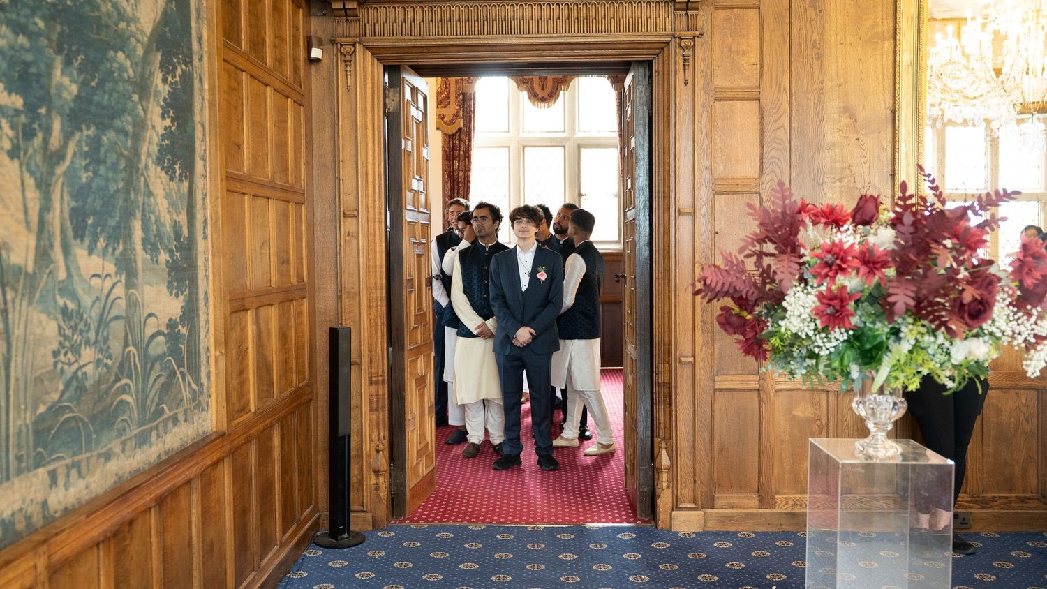 Wedding guests in traditional South Asian attire gathered in elegant wood-paneled venue doorway.