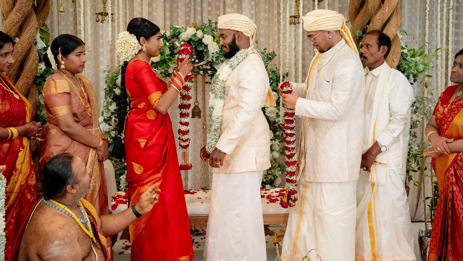 Traditional South Indian wedding ceremony with bride in red saree and groom in white sherwani exchanging varmala.