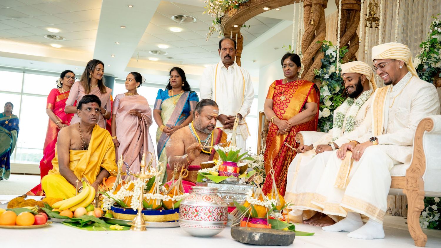Traditional South Indian wedding ceremony with family gathered around ritual offerings, flowers, and sacred items on a decorated altar.