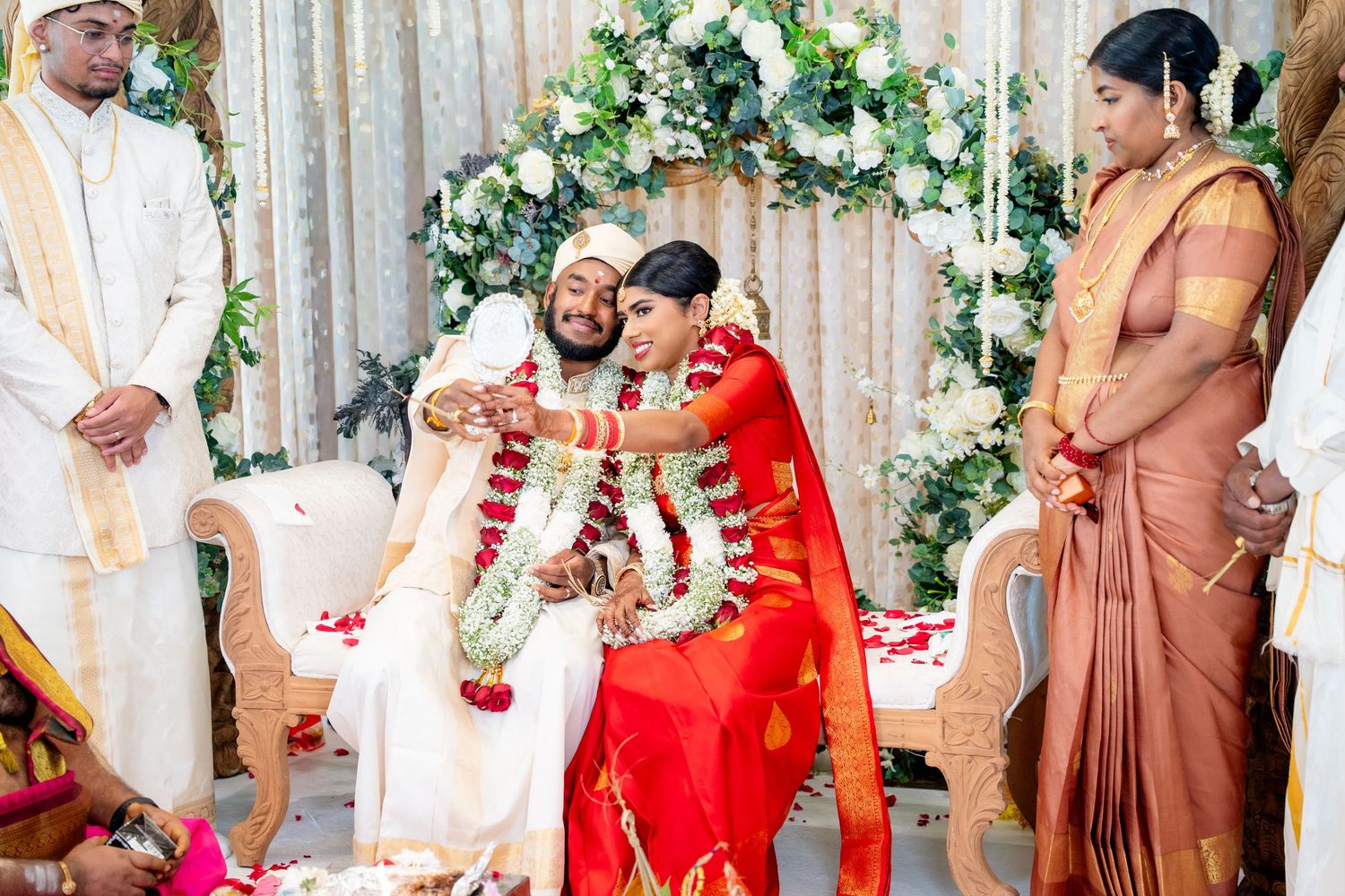 Groom places garland on bride during traditional South Indian Hindu wedding ceremony with attendants.