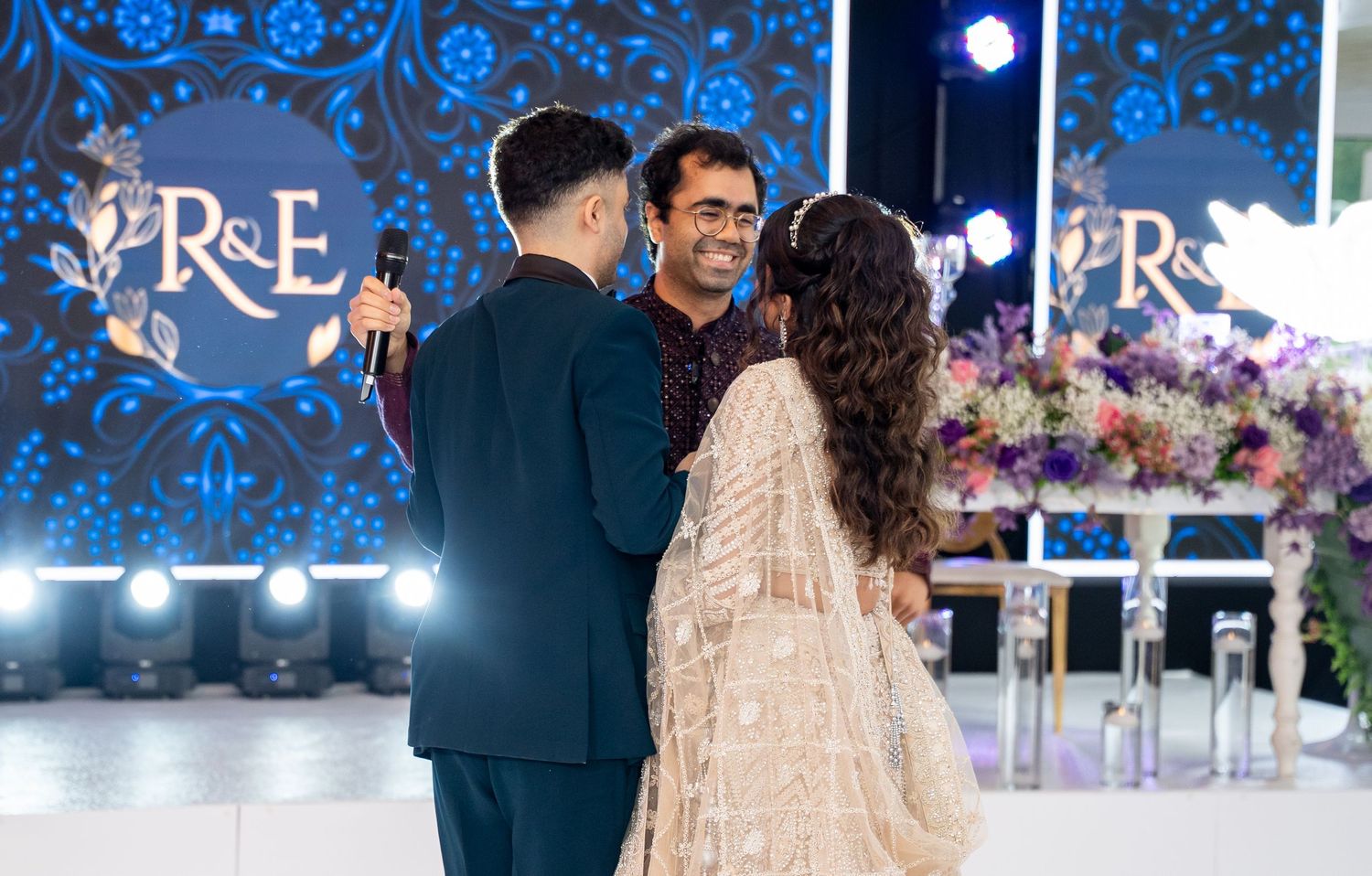 Groom and guest sharing a warm moment with bride in gold lehenga at wedding reception on stage.