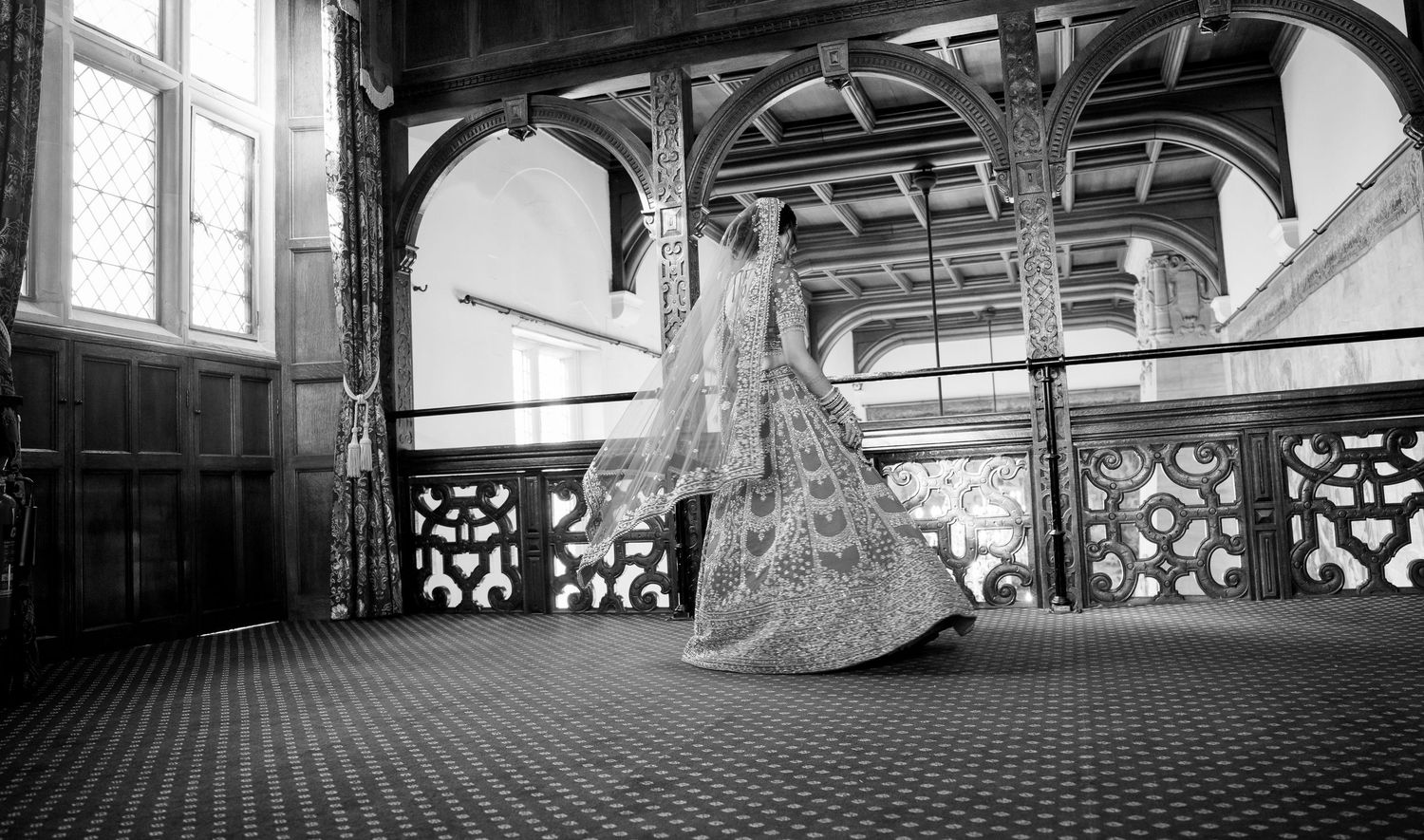 Black and white photo of Indian bride twirling in ornate wooden hall.