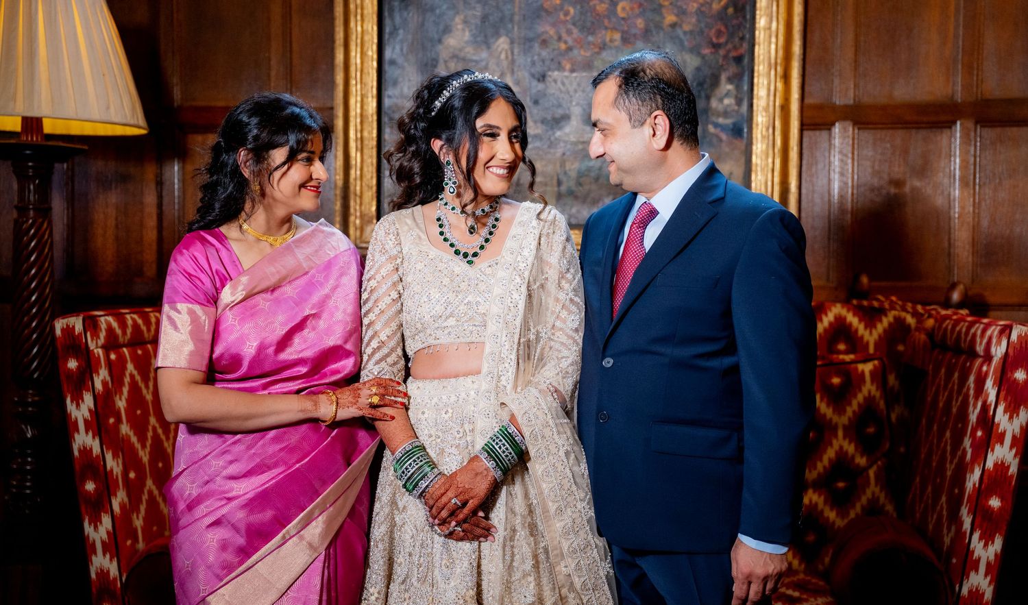 Indian family in traditional attire smiling together in an elegant wood-paneled room during a wedding celebration.
