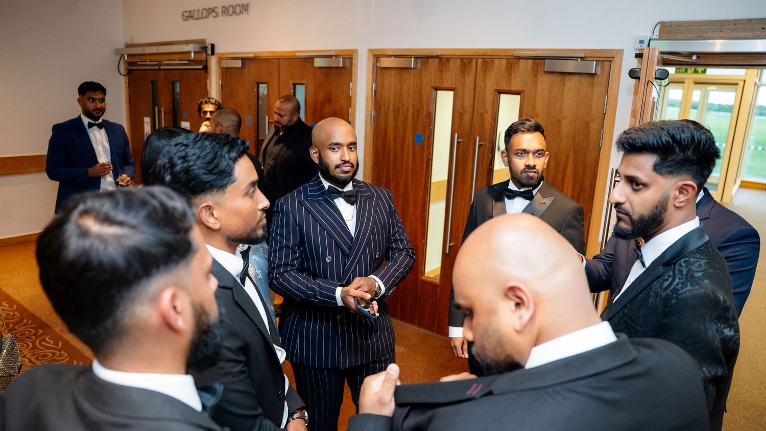 Men in formal attire including pinstripe suit gather in conversation at a wedding venue.