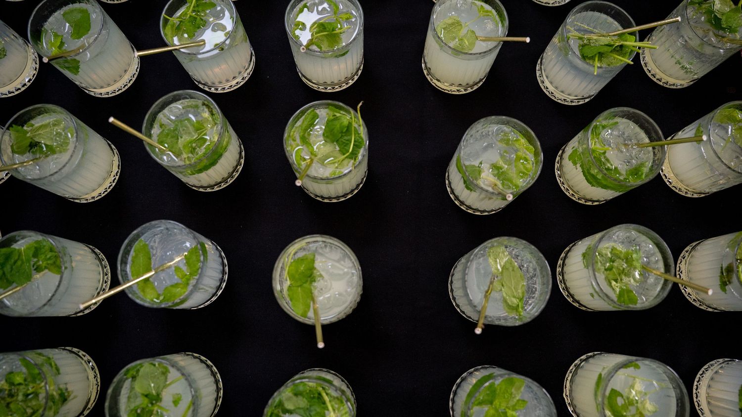 Overhead view of rows of mojito cocktails garnished with mint on a dark surface.
