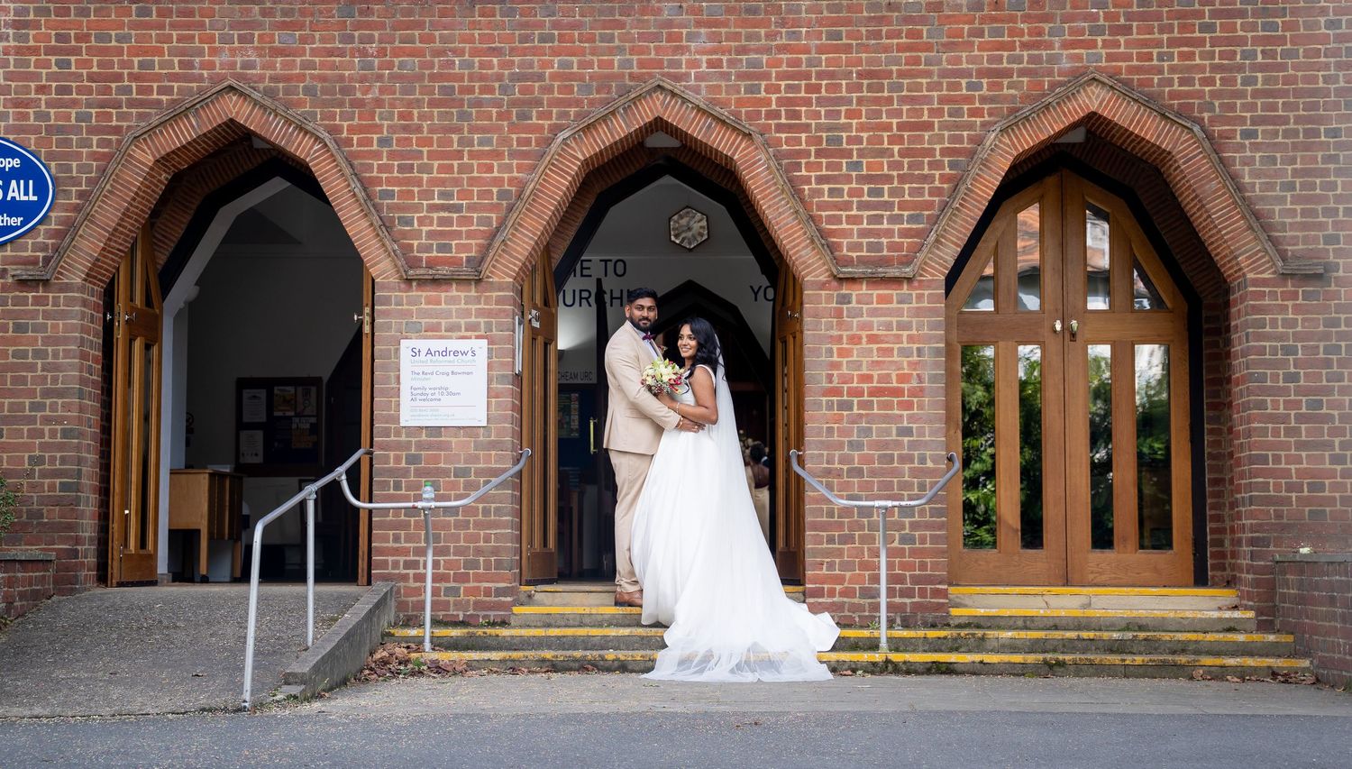 Bride and groom embracing at the entrance of a red brick church on their wedding day.