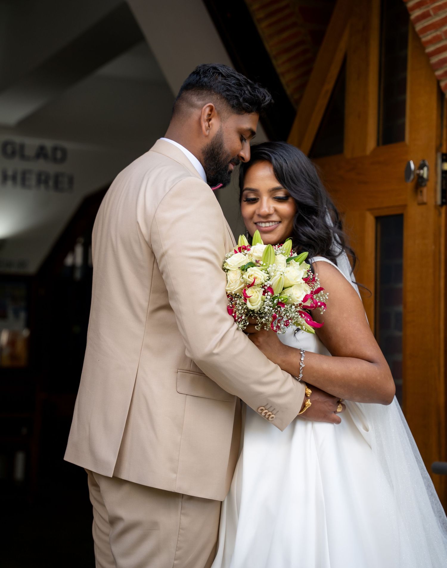 Bride and groom share a tender embrace outside a church, bride holding a colorful bouquet in a white wedding gown.