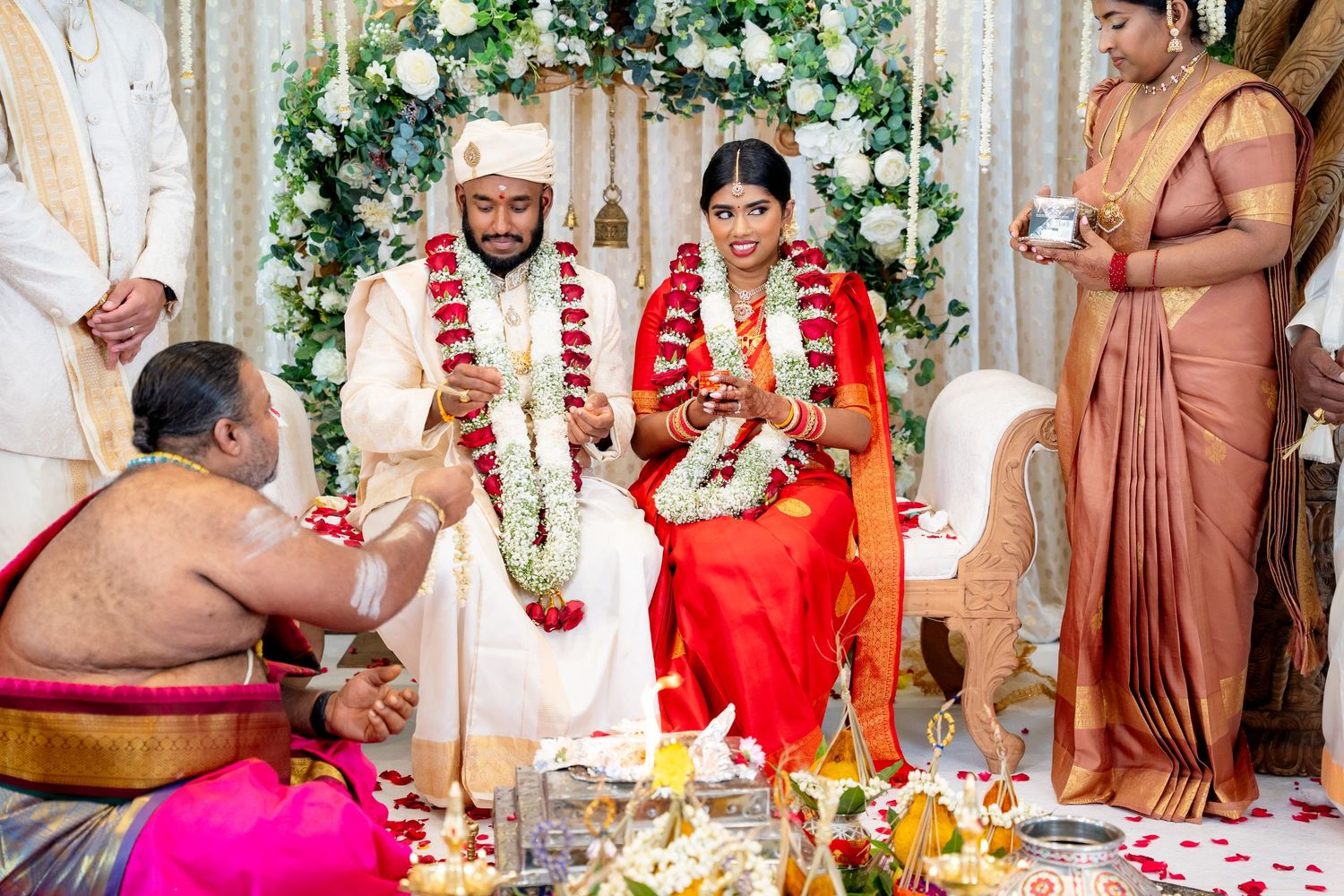 Bride and groom participate in traditional Hindu wedding rituals with priest and flower petals.