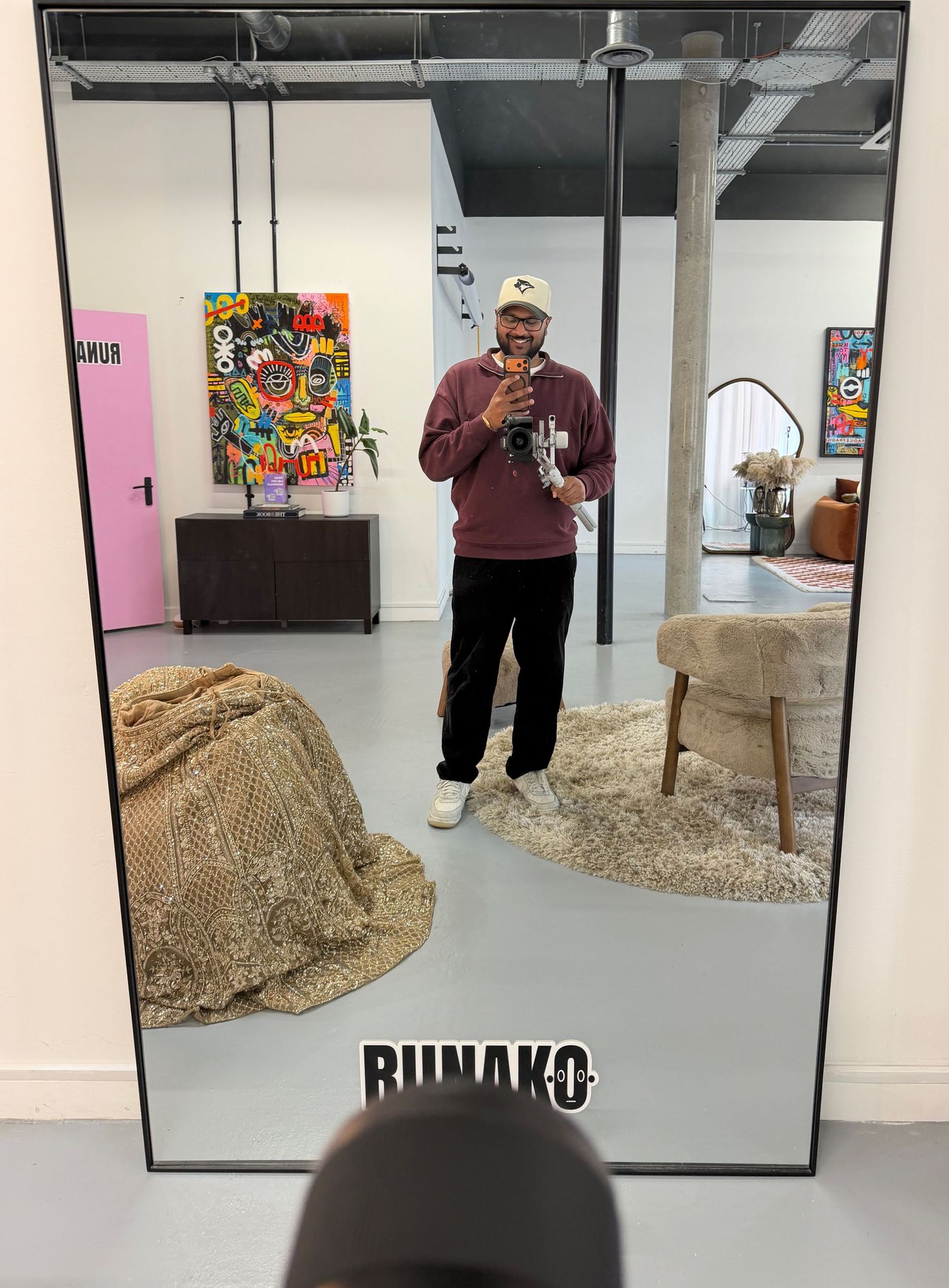 Man in burgundy sweatshirt smiles in mirror selfie at Runako creative studio space.