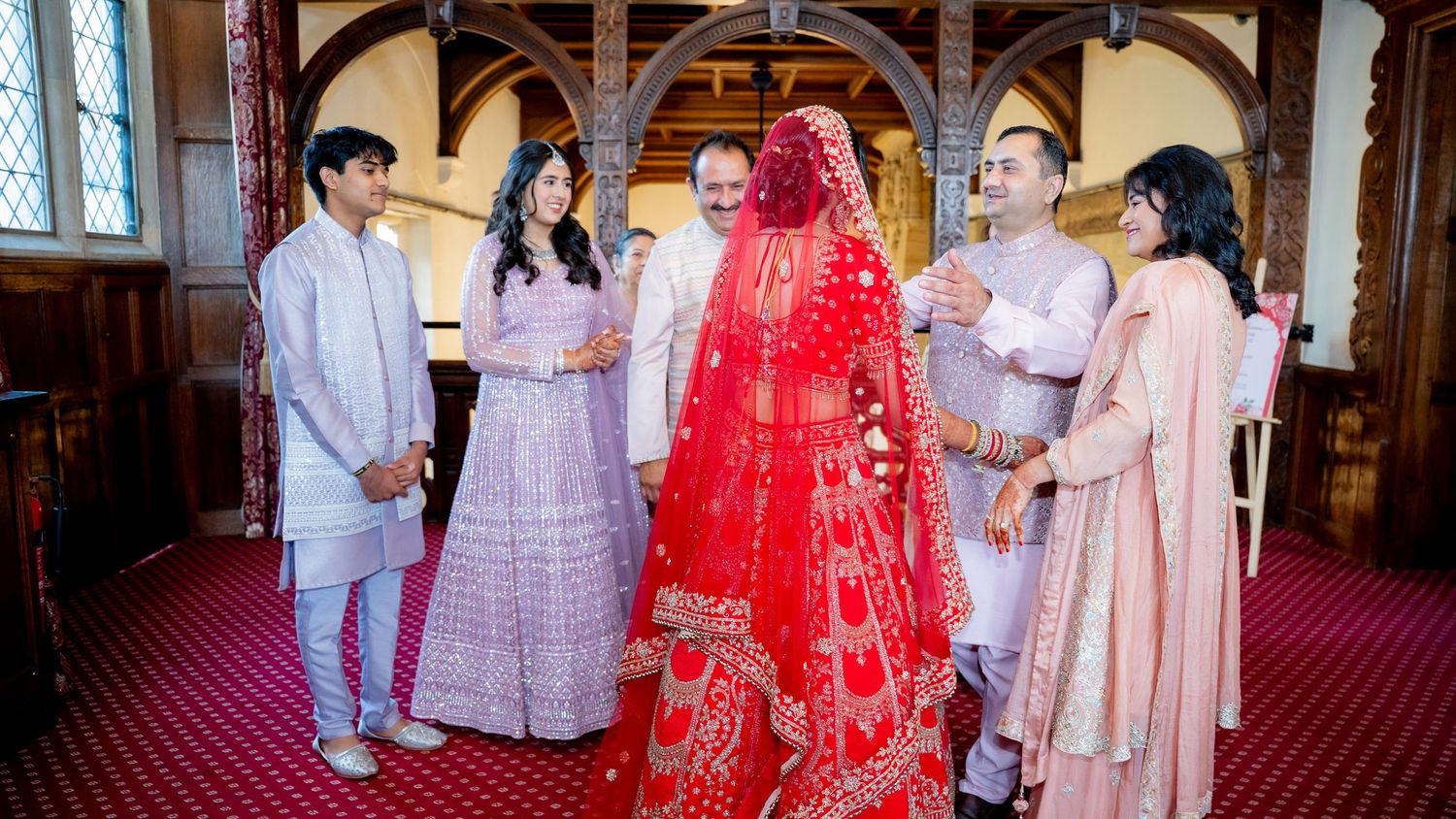 Indian bride in red bridal lehenga with family members in traditional outfits at wedding ceremony.