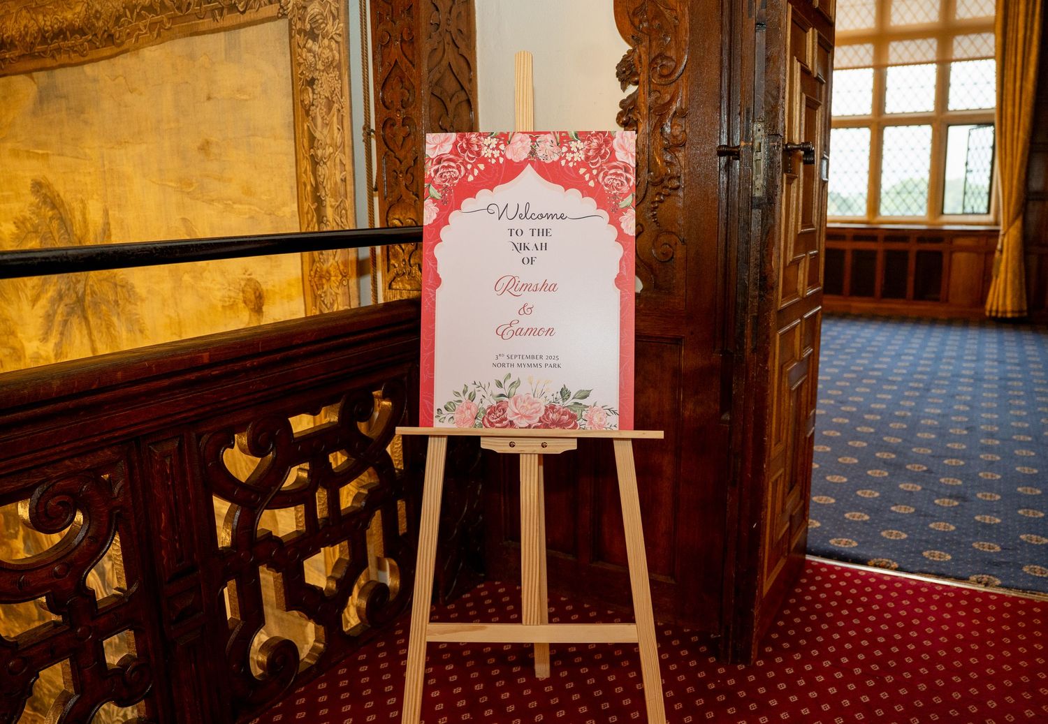 Elegant red and white Indian wedding welcome sign on a wooden easel in an ornate venue.