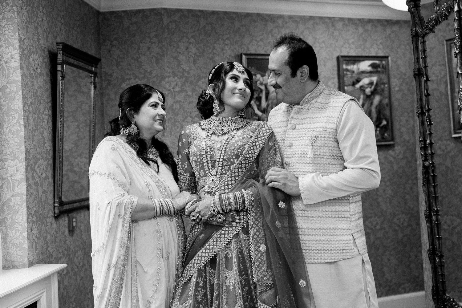 Black and white photo of a South Asian bride in traditional bridal attire with two guests at a wedding ceremony.