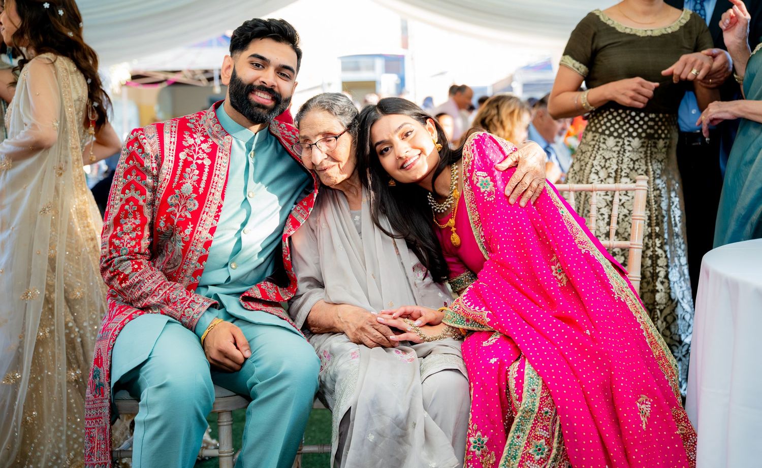 Indian groom in turquoise sherwani poses with elderly woman and bride in pink lehenga.