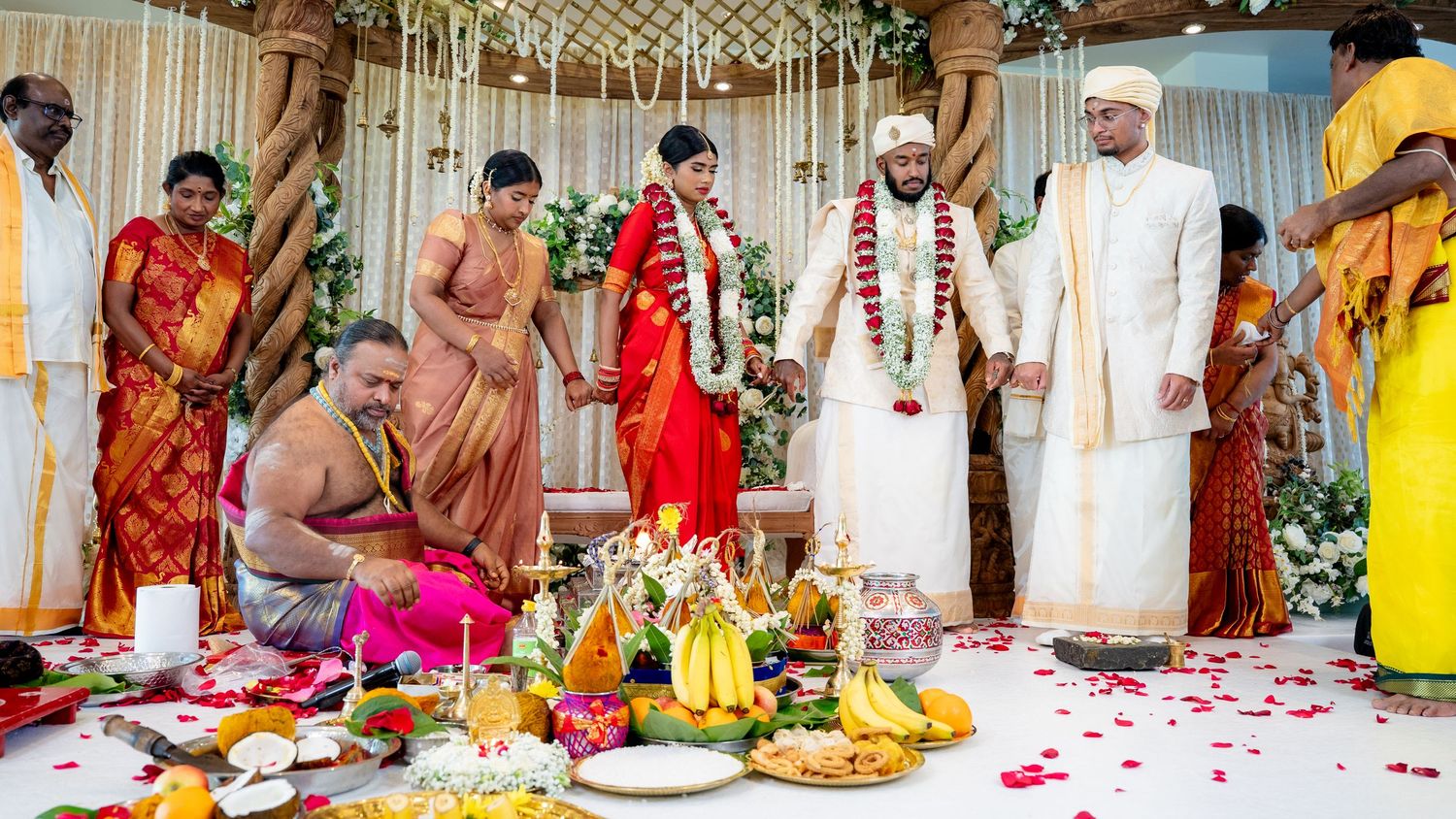 South Indian wedding ceremony with priest, bride in red saree, and groom in white performing traditional Hindu marriage rituals.