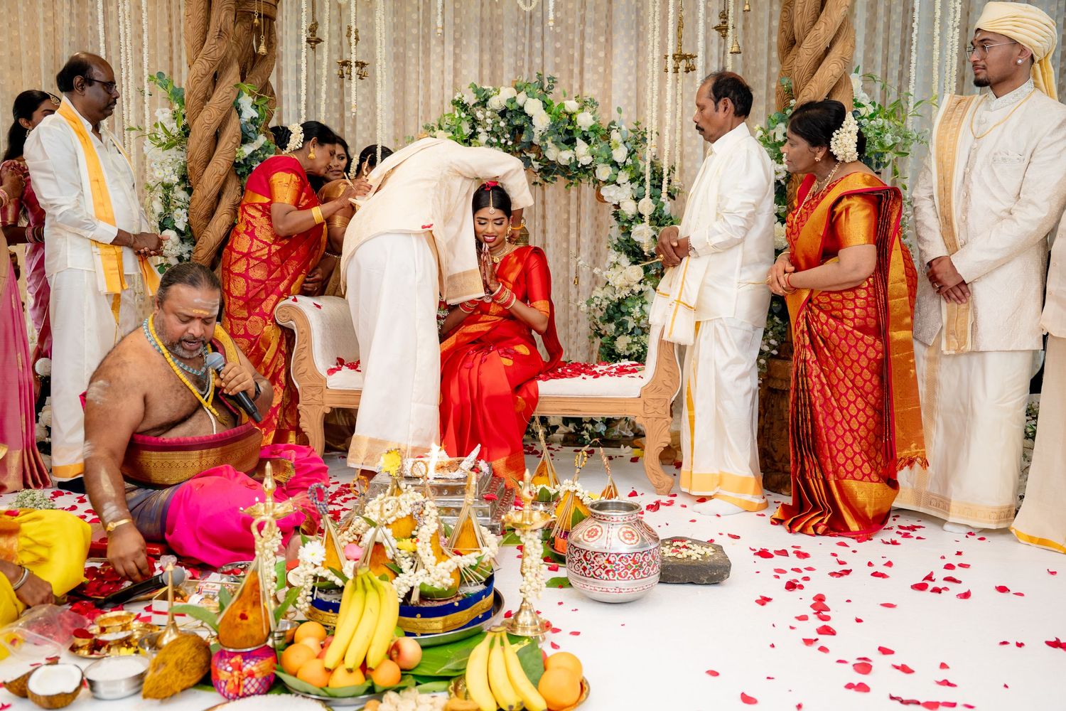 Traditional South Indian wedding ceremony with priest, couple, and family on flower-petal-adorned mandap stage.