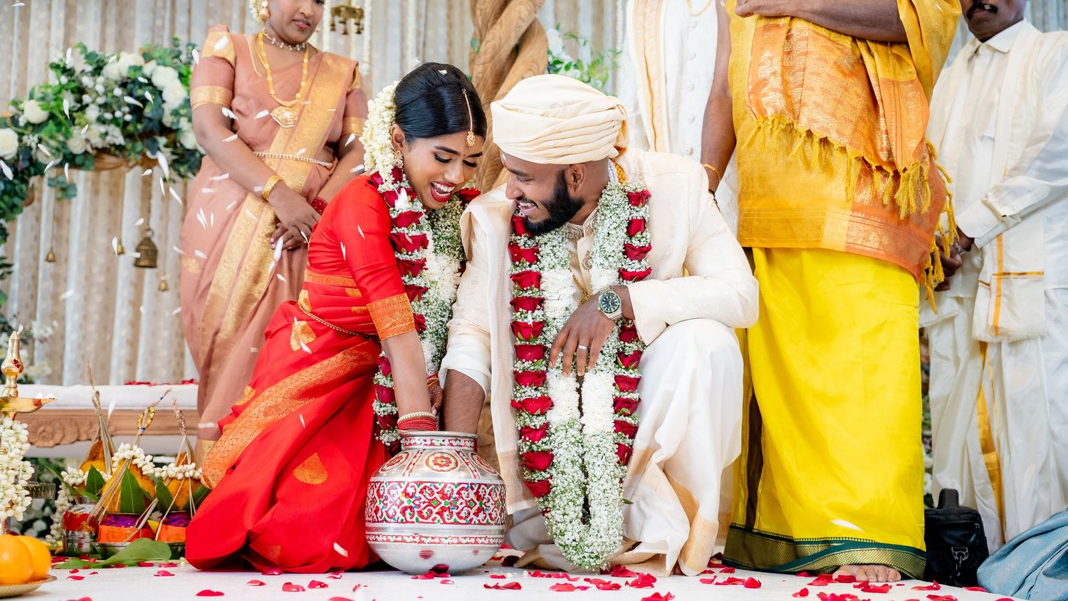 Bride in red saree and groom in white exchanging garlands during traditional Hindu wedding ceremony.