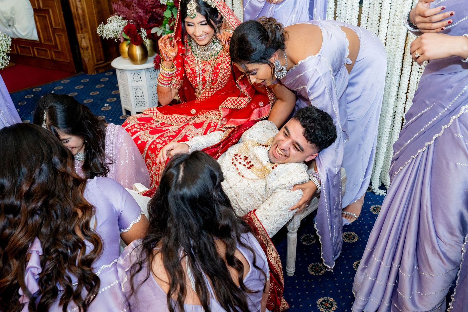 Indian bride and groom surrounded by bridesmaids in lavender dresses during a traditional wedding ceremony.