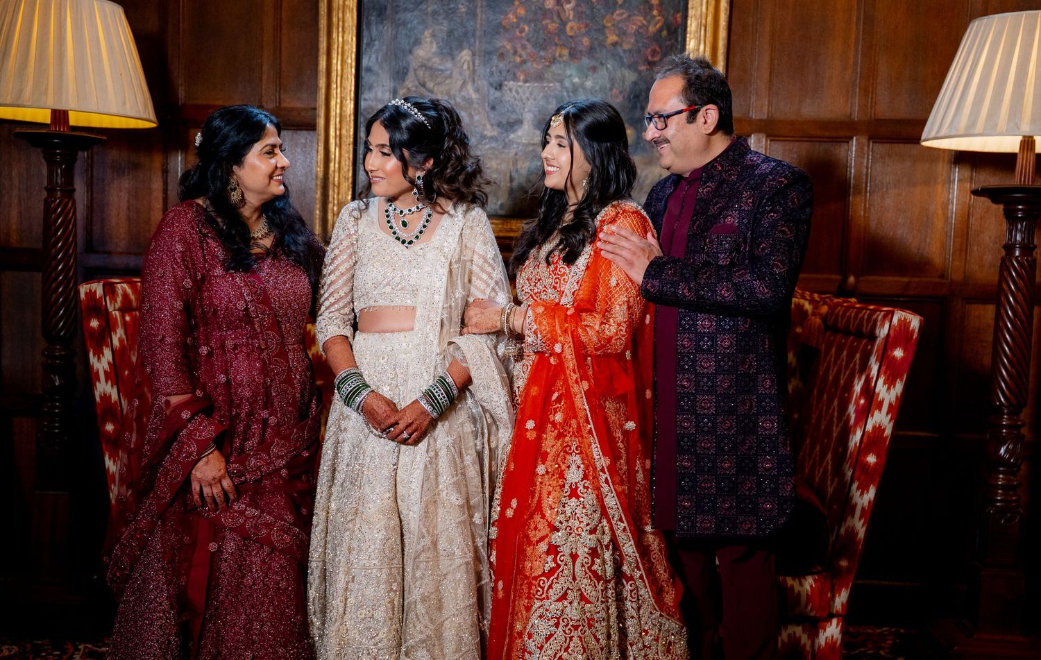Four guests in vibrant Indian wedding attire pose together in an elegant wood-paneled room.
