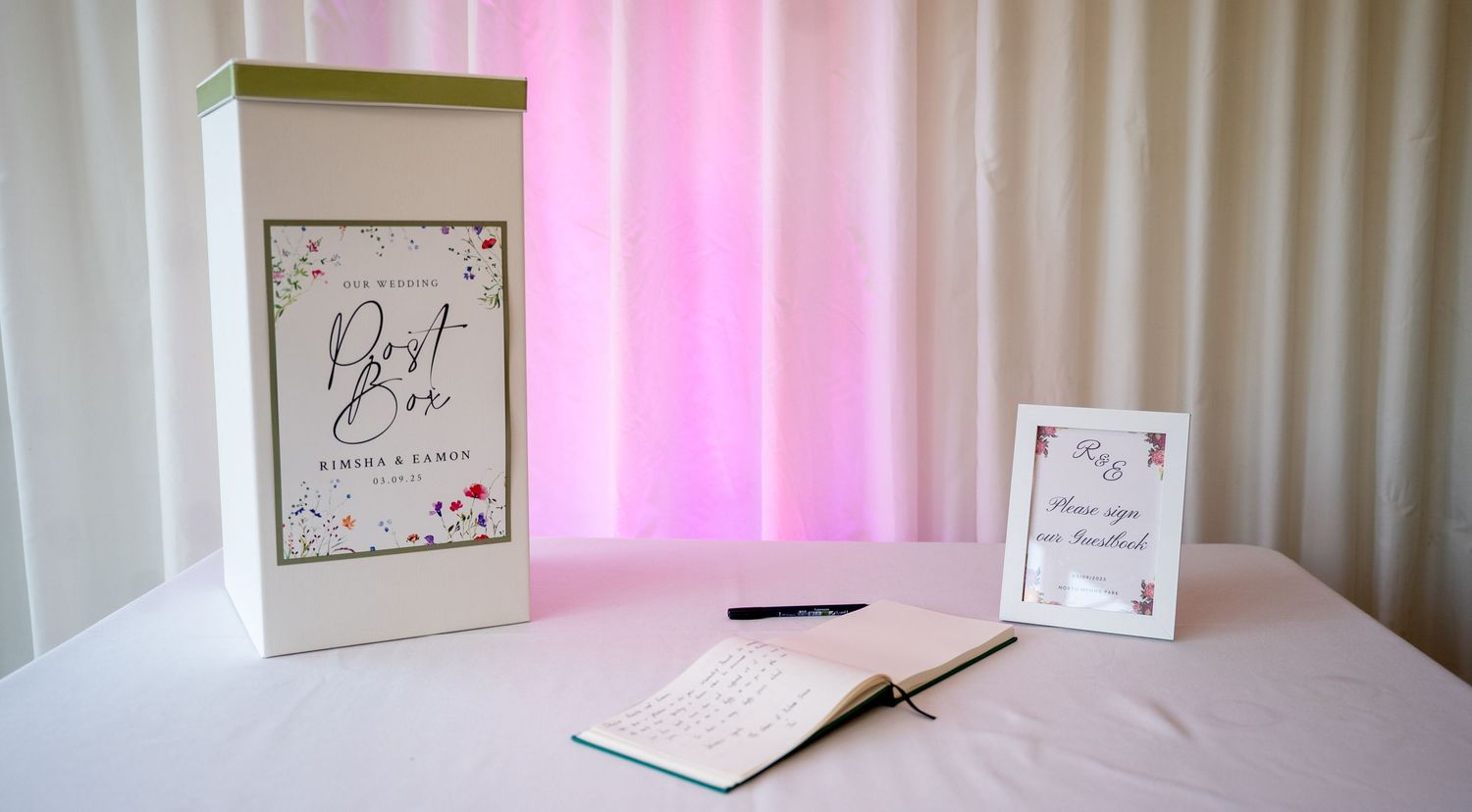 Elegant wedding card box and guest book on a white table with a pink curtain backdrop at a reception.