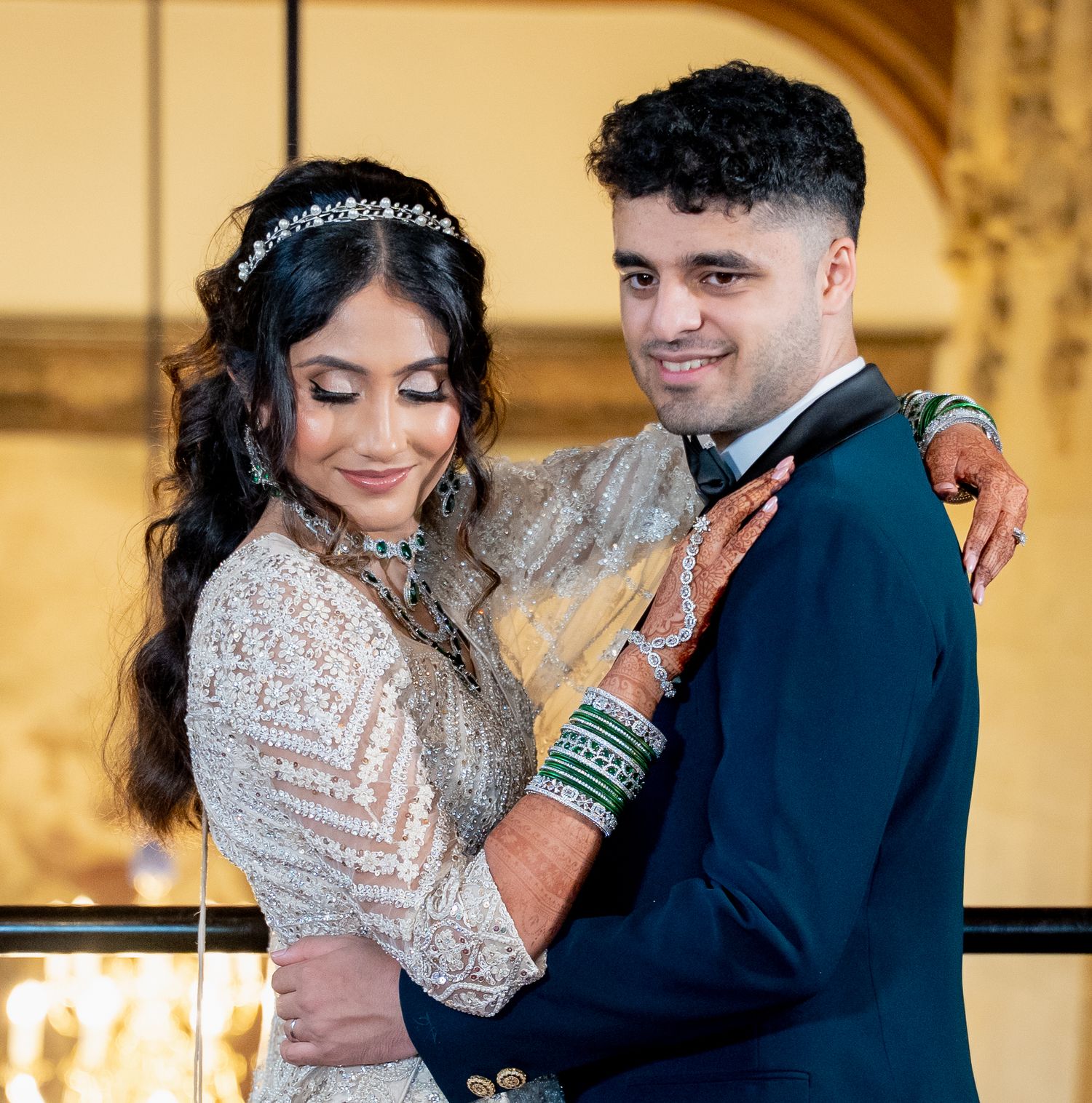 South Asian bride in white embroidered lehenga with green bangles smiles with groom in navy suit at wedding.