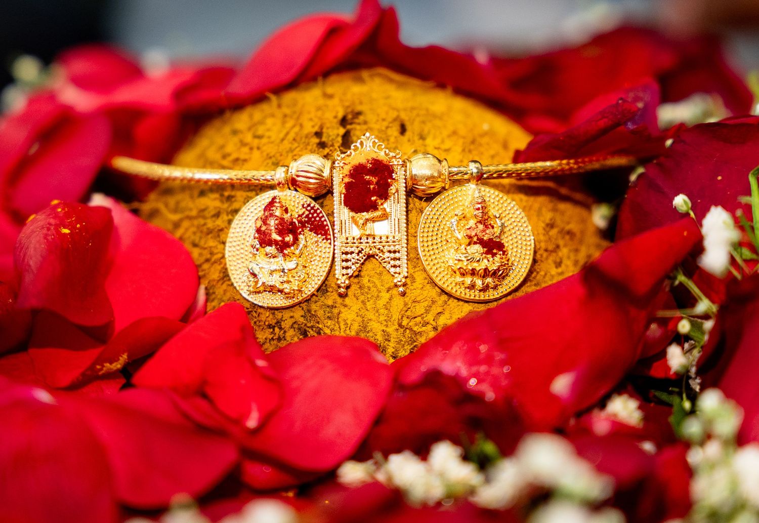 Gold bridal jewelry with red gemstones displayed on turmeric powder surrounded by red rose petals.