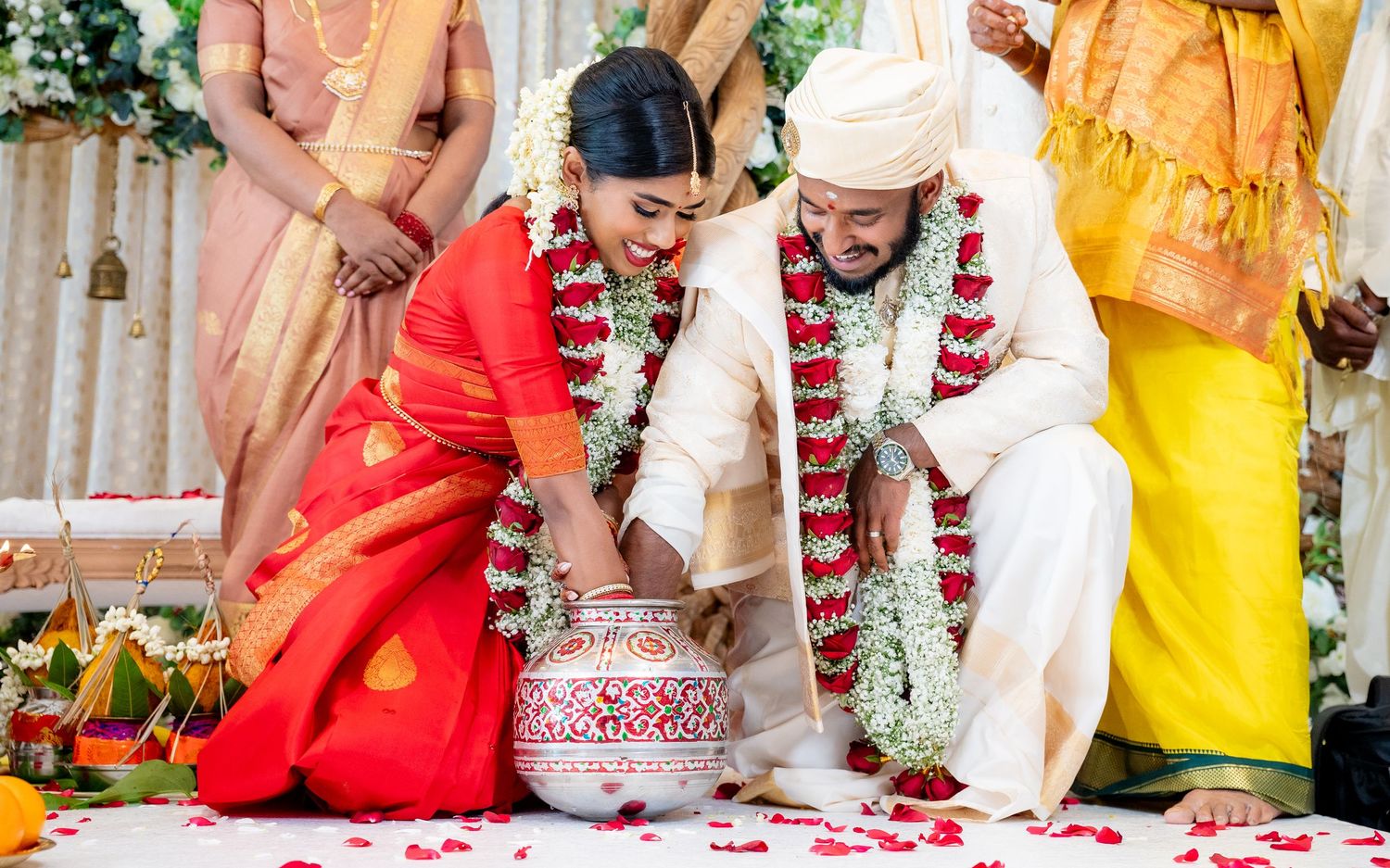 Indian couple in traditional attire performing wedding ceremony ritual with floral garlands and red rose petals.
