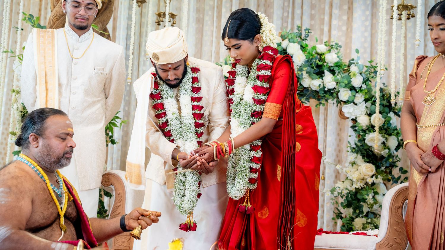 Hindu wedding ceremony couple exchanging garlands at decorated altar with priest officiating.