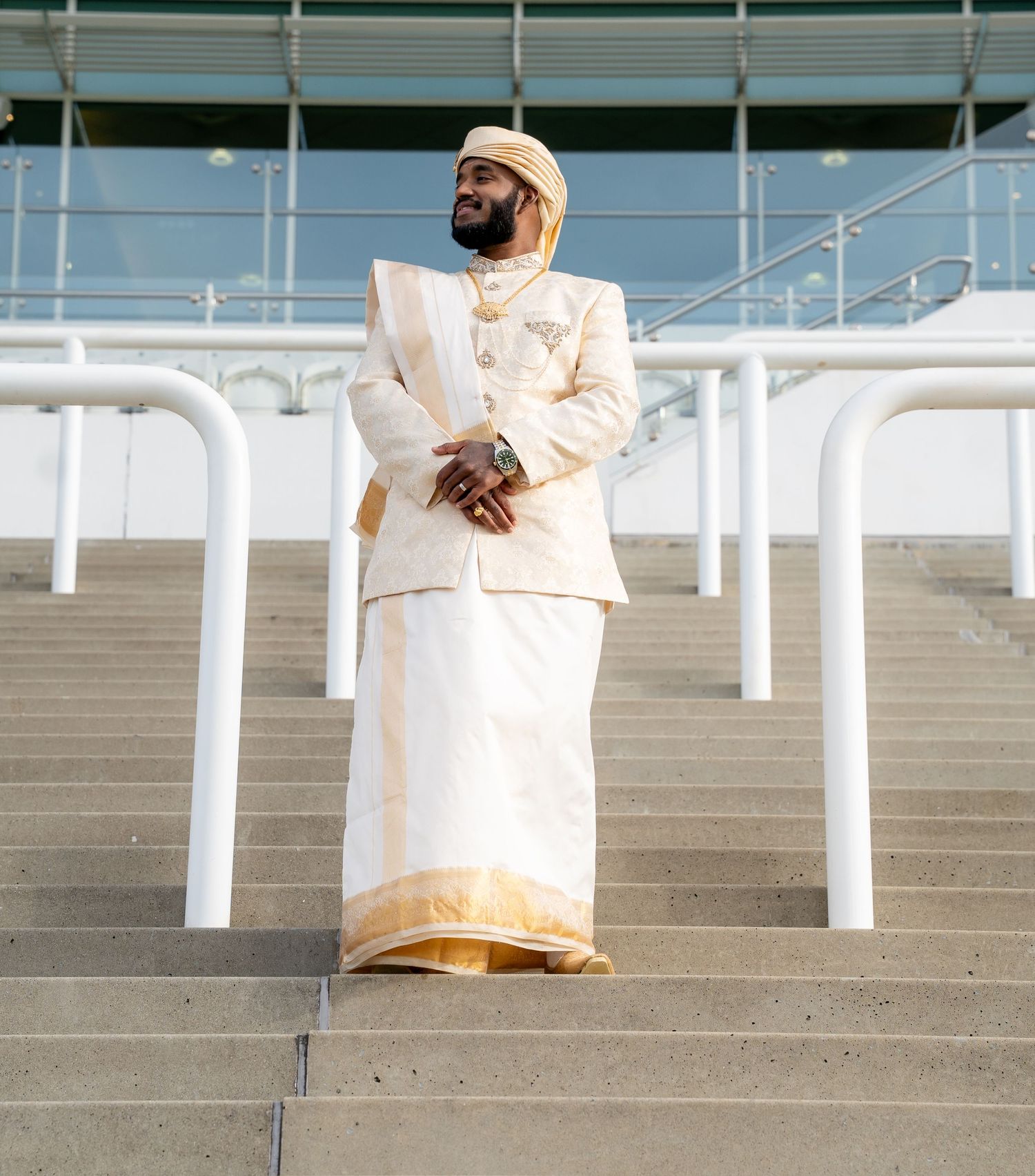 Man in white and gold traditional South Asian outfit standing proudly on stadium steps.