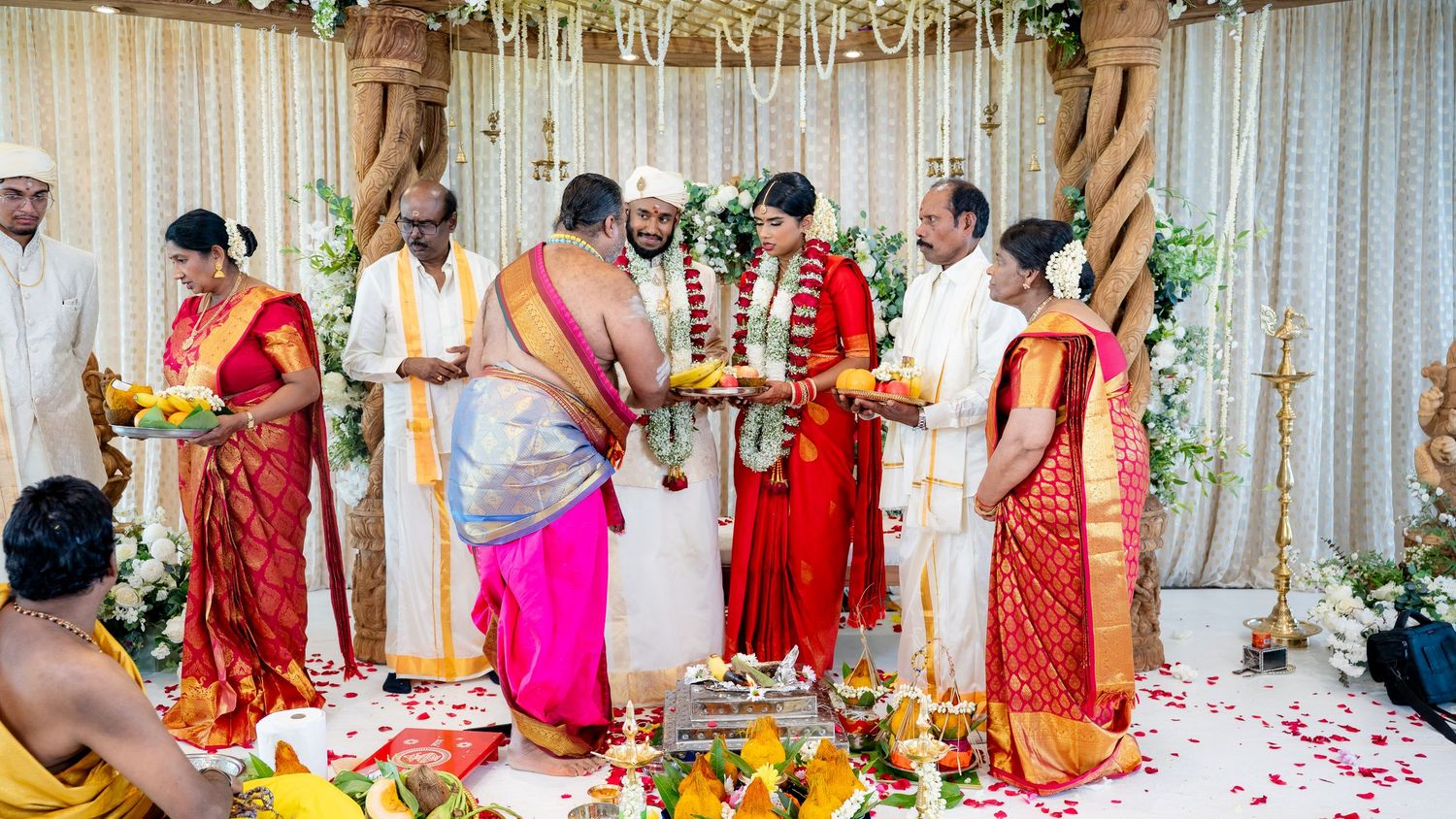 Traditional South Indian wedding ceremony with family performing rituals around bride in red saree and groom in white.