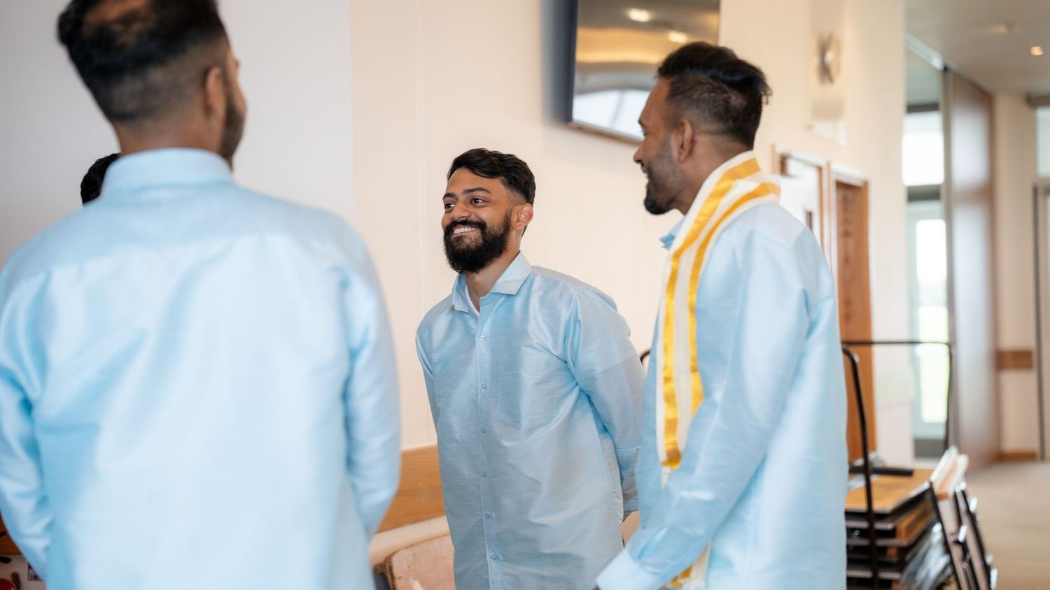 Indian groom in light blue kurta laughs joyfully with groomsmen in matching outfits.