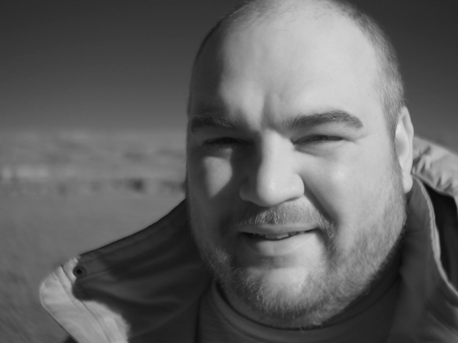 Black and white close-up portrait of smiling man outdoors in winter.