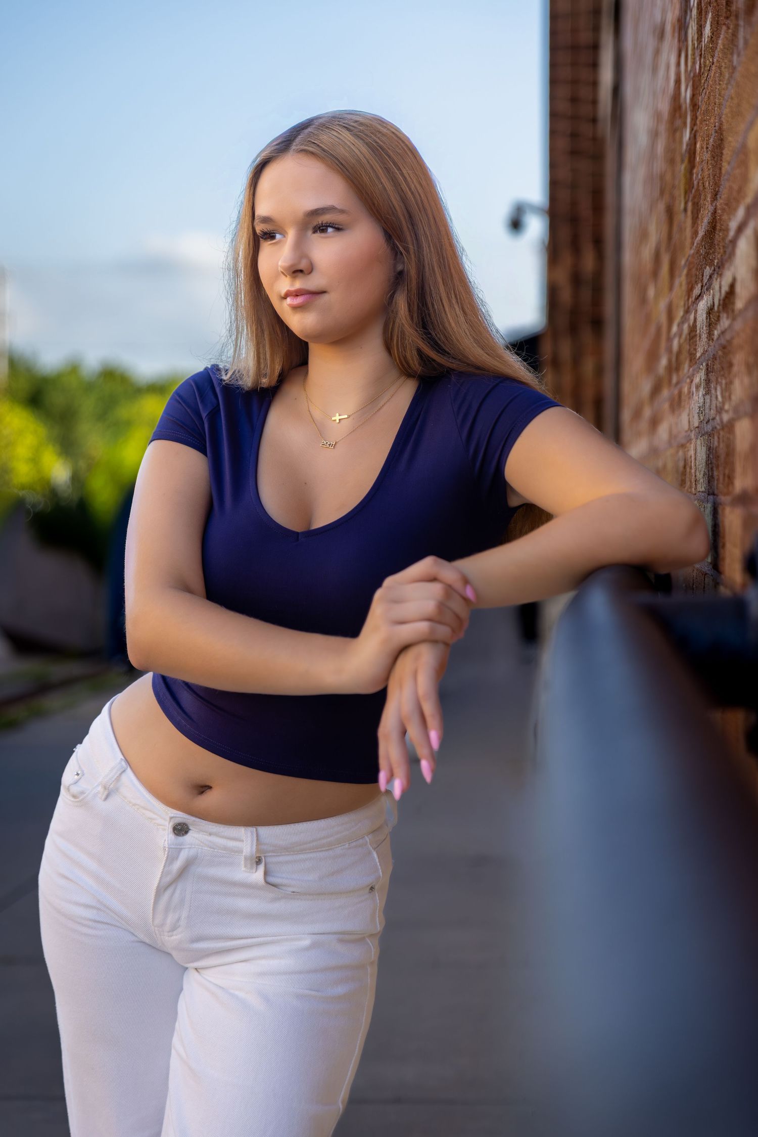 Young woman in navy crop top and white jeans leaning against railing outdoors.