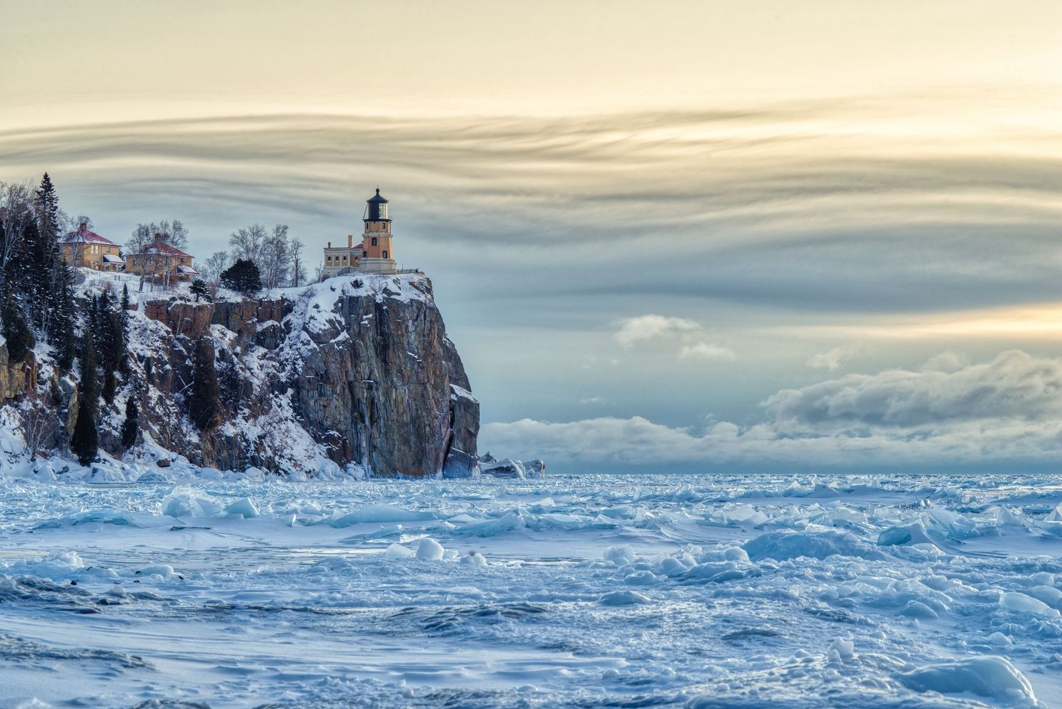 Split Rock Lighthouse surrounded by frozen Lake Superior waves under dramatic winter clouds.