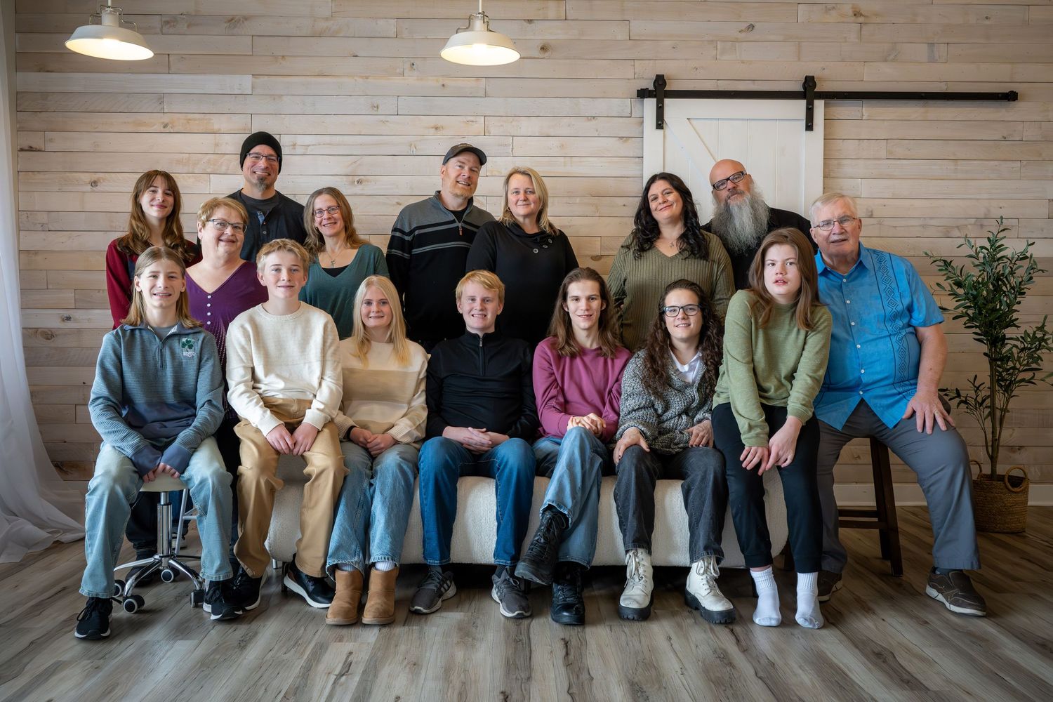 Large family group portrait with adults and children posing together in a modern rustic room with shiplap walls.