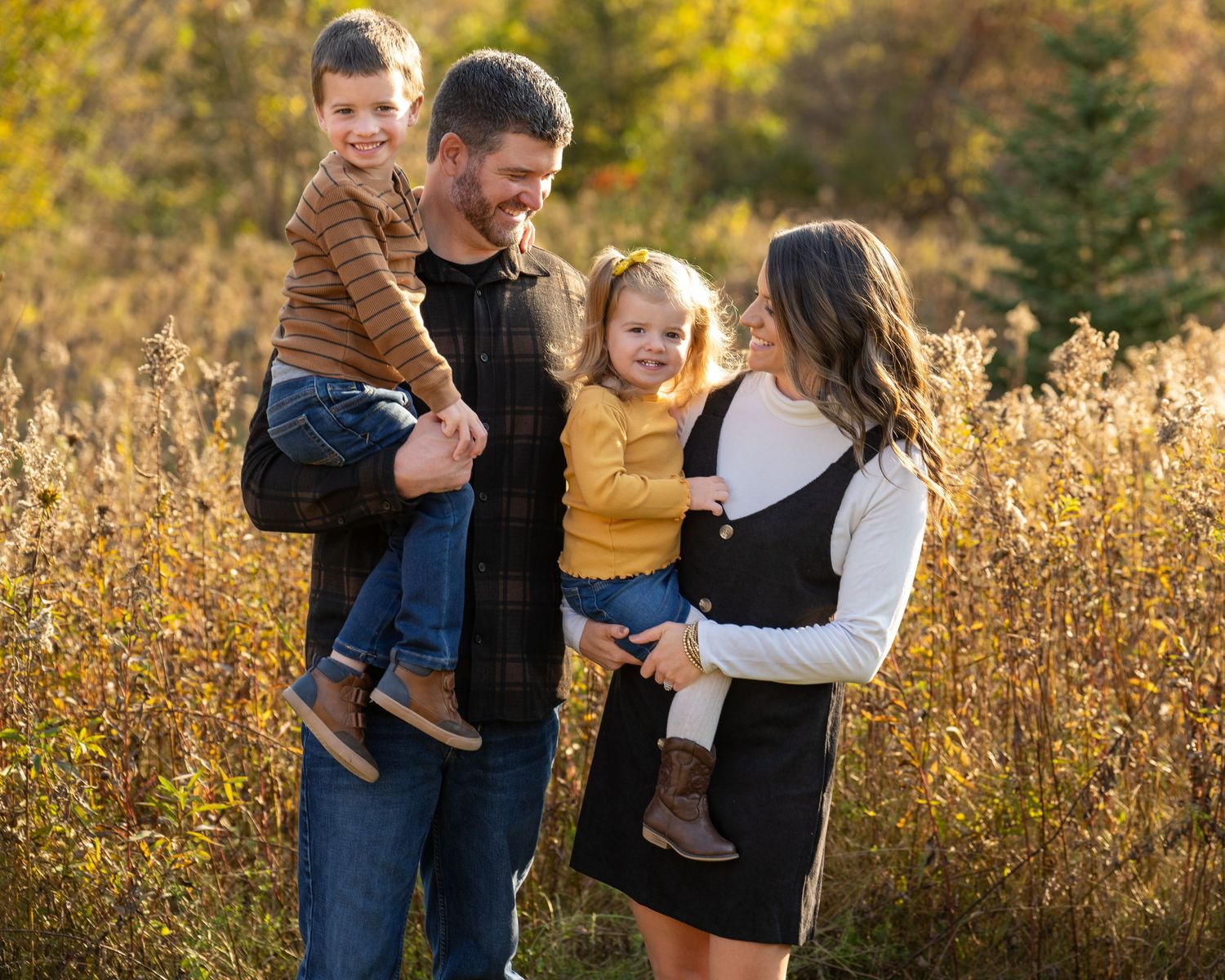 Happy family with two young children posing in autumn field with colorful foliage.