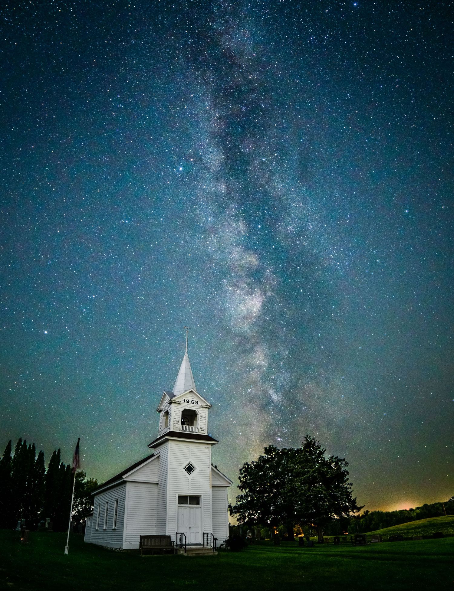 White country church beneath a stunning Milky Way galaxy on a clear summer night.