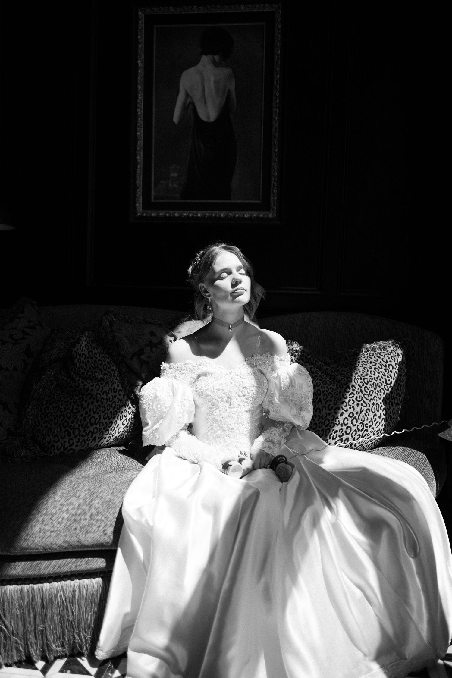 Bride in white gown sitting on sofa in dramatic black and white portrait with painting on wall at The Floridian Social St. Petersburg.