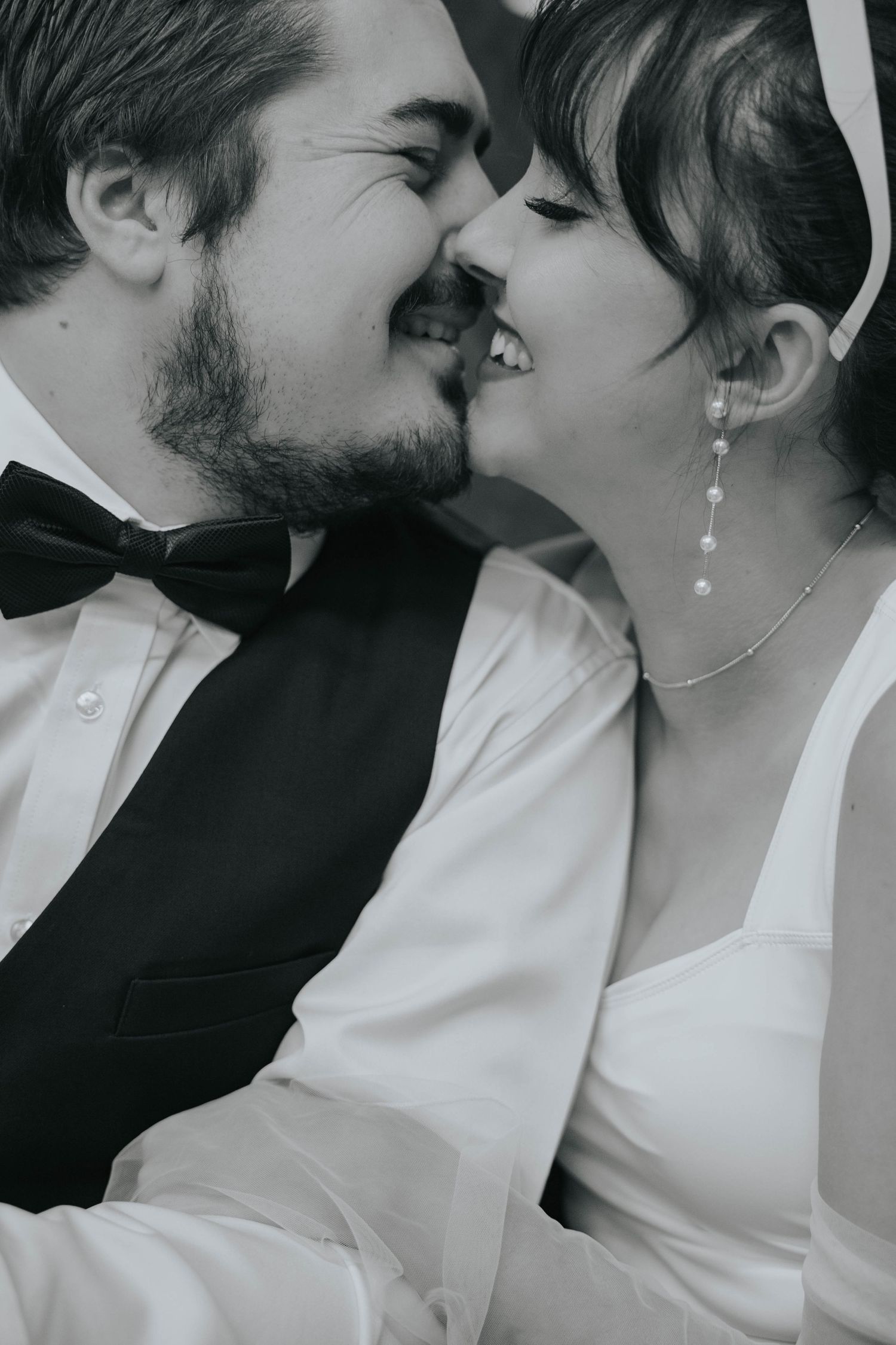 Black and white close-up of laughing bride and groom nearly kissing on wedding day.